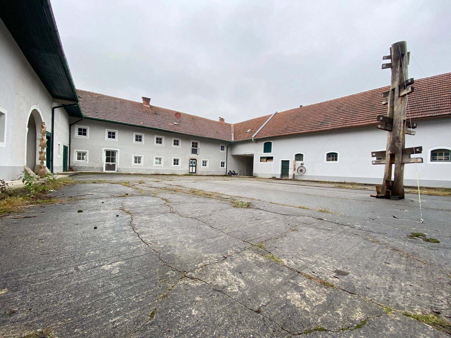 Großer Innenhof, umgeben von Gebäudeteilen, mit rissigem Betonboden und einem hölzernen Wegweiser.