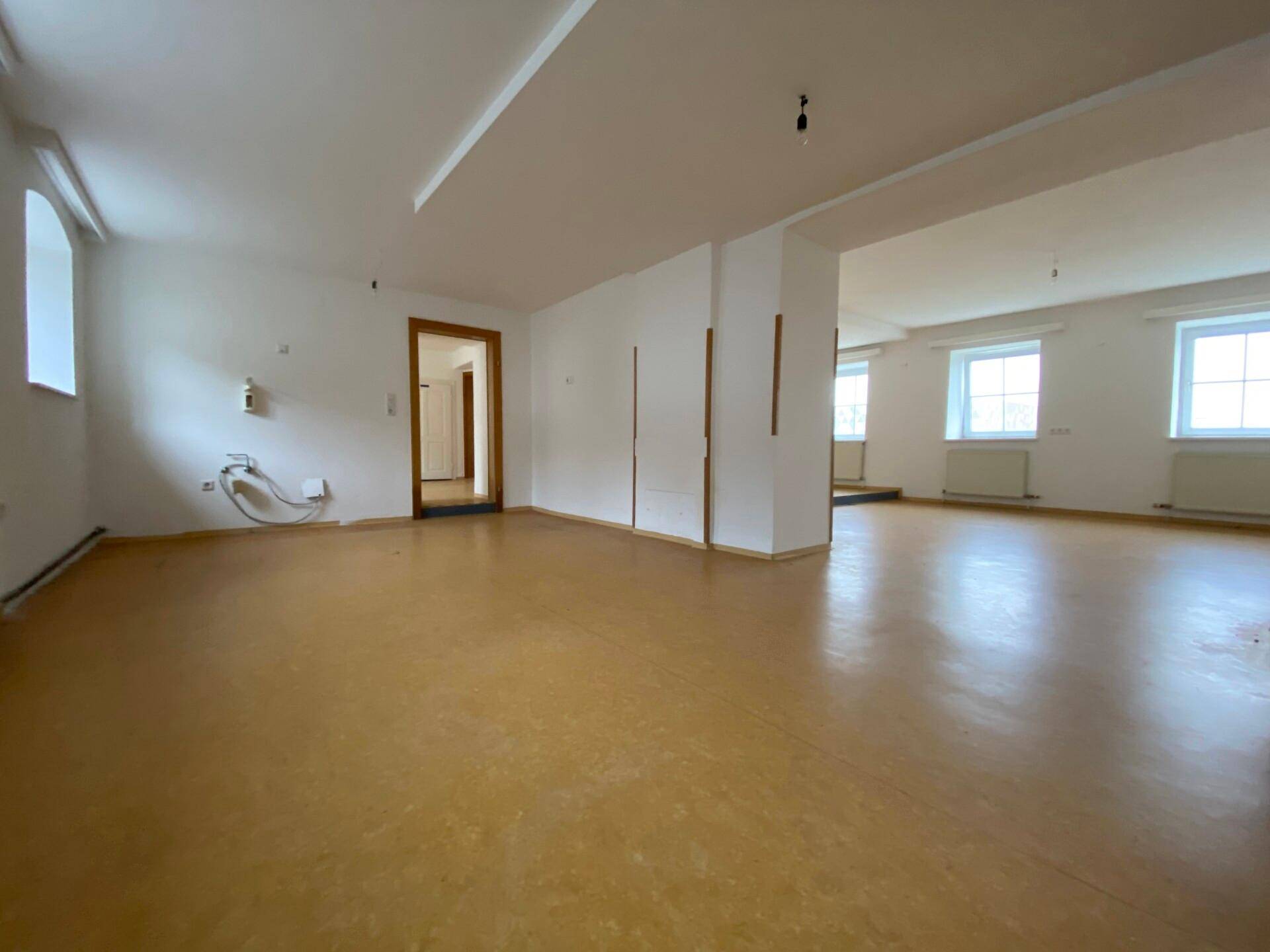 Geräumiger, leerer Innenraum mit braunem Linoleumboden, weißen Wänden und Holztürrahmen, bereit zur Nutzung.