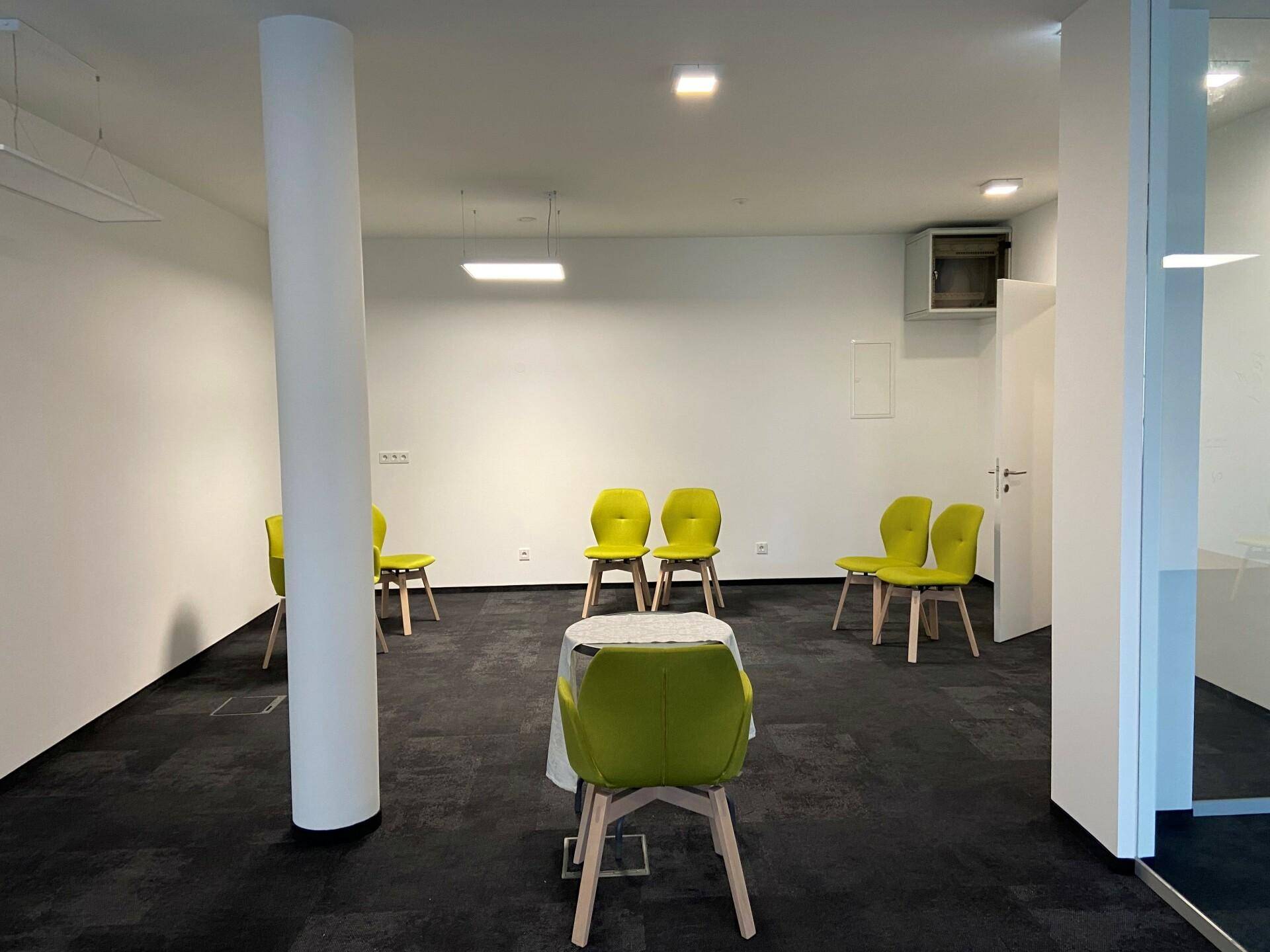 Geräumiger Bürobereich mit einer Säule und modernen, limettengrünen Stühlen, ideal für Besprechungen oder Wartebereiche.