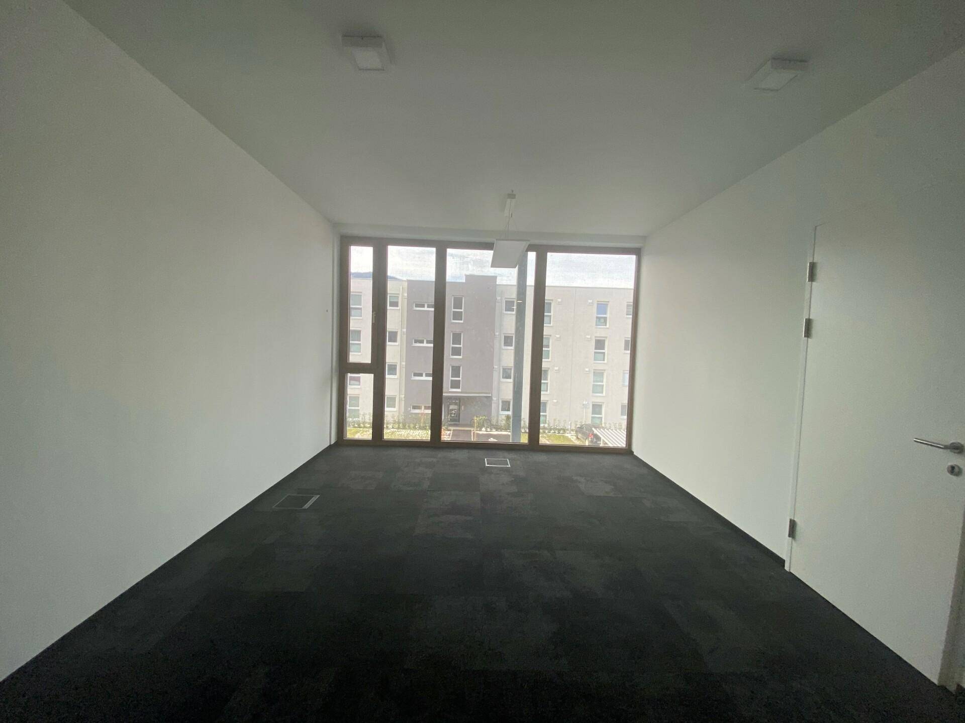 Leerer Büroraum mit großen Fenstern, die eine weite Aussicht bieten und den Raum mit natürlichem Licht füllen.