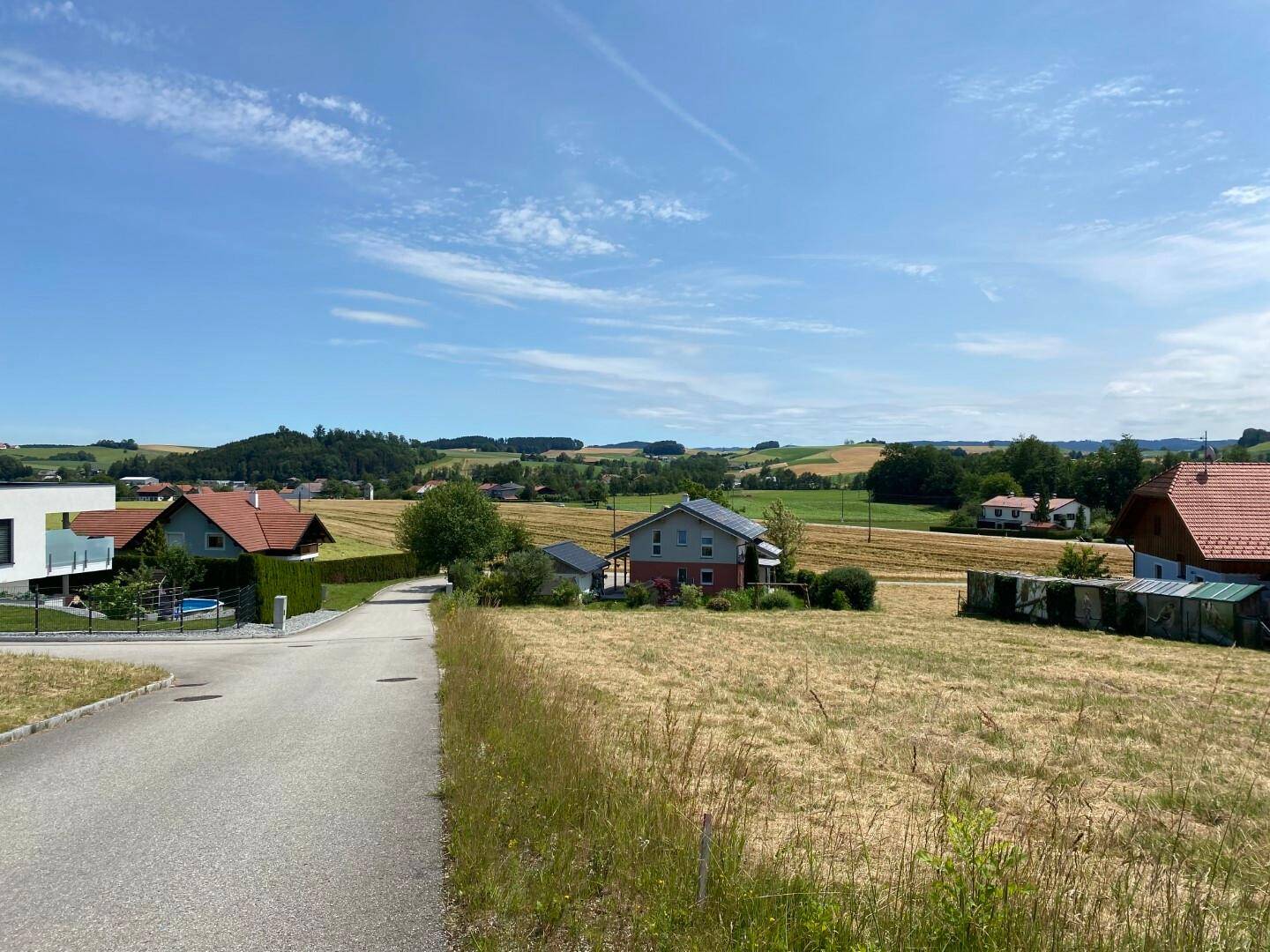 Ländliche Wohngegend mit Straße, Häusern und weiten Feldern unter blauem Himmel.