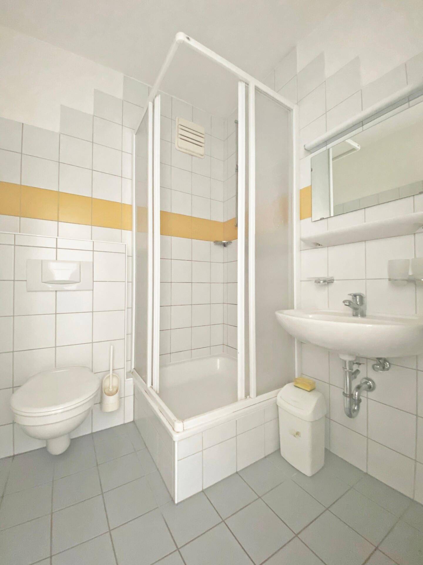 Funktionales Badezimmer mit Dusche, WC und Waschbecken, gefliest in Weiß und Gelb.