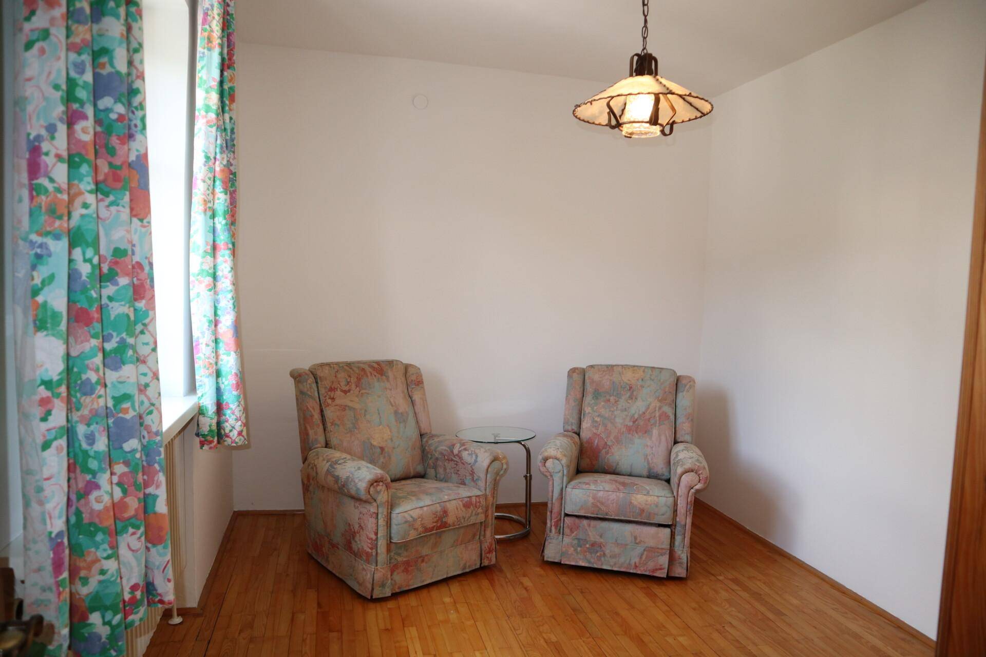 Heller Raum mit zwei bequemen Sesseln, Holzboden und farbenfrohen Vorhängen.