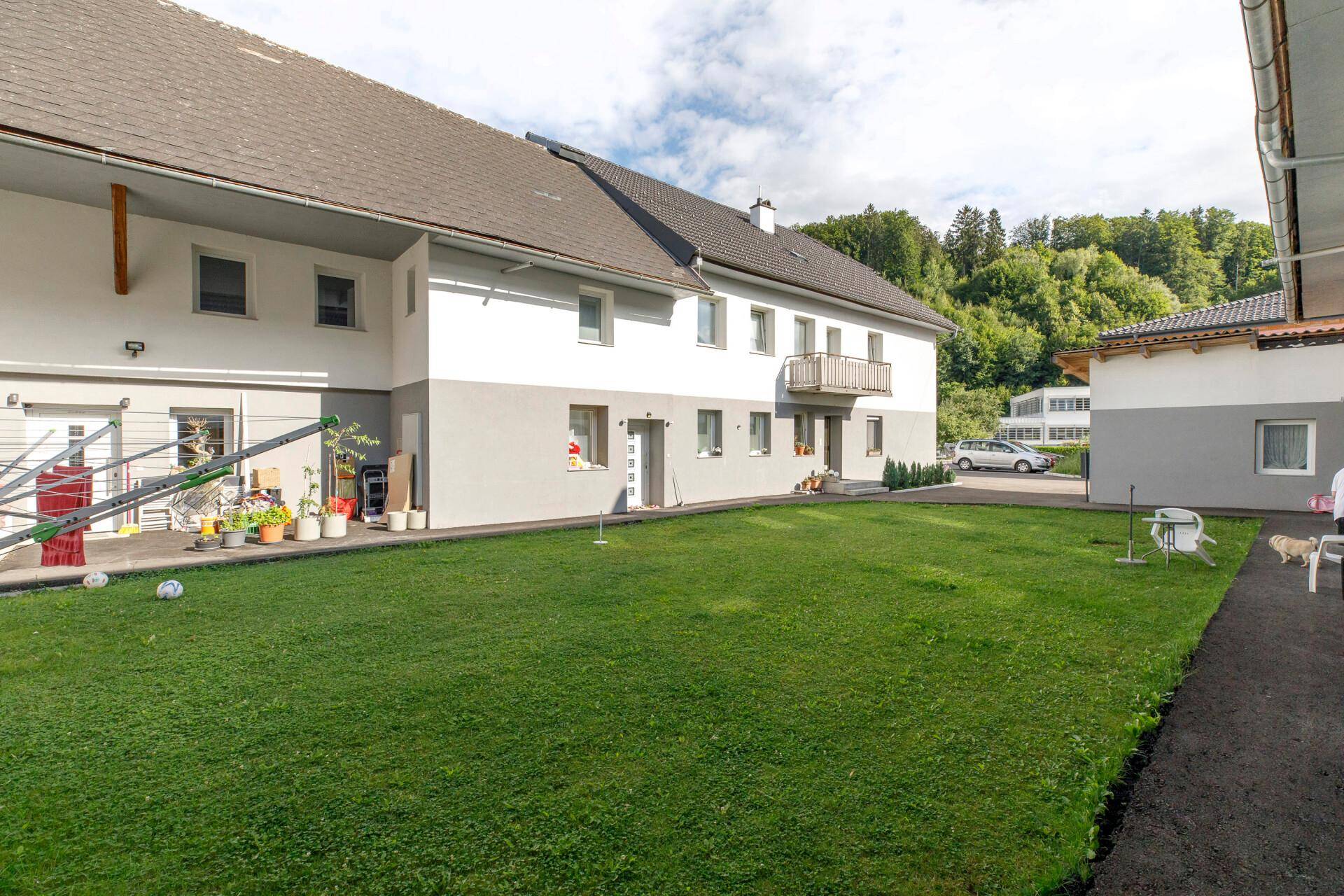 Gepflegter Rasenbereich vor einem modernen Wohngebäude mit kleinem Balkon und grüner Umgebung.