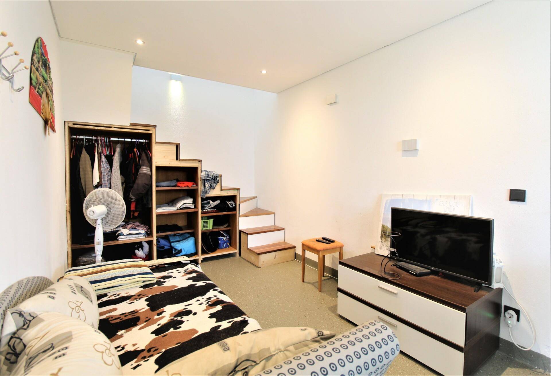Gemütlicher Wohnbereich mit Schlafsofa, Fernseher und offener Treppe zu einem oberen Bereich, inklusive Kleiderschrank.