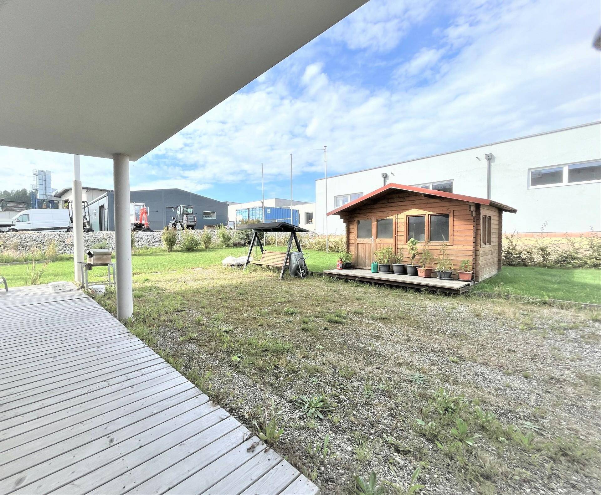 Gartenbereich mit einer kleinen Holzhütte, Schaukel und Rasenfläche, angrenzend an eine überdachte Terrasse.