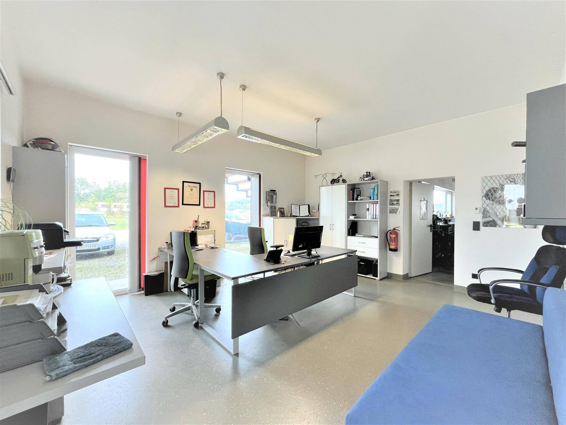 Geräumiges Büro mit mehreren Schreibtischen, Bürostühlen und einer blauen Couch, gut beleuchtet durch große Fenster.
