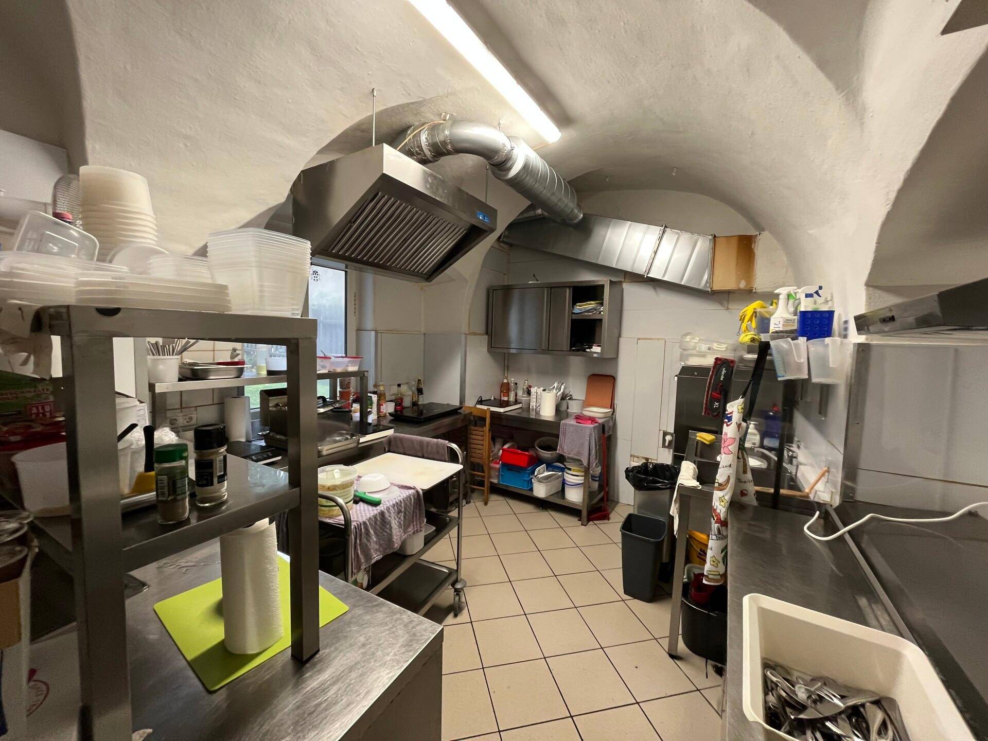 Gewerbliche Küche mit Edelstahlflächen, Industriekapuze und gefliestem Boden unter einer gewölbten Decke.