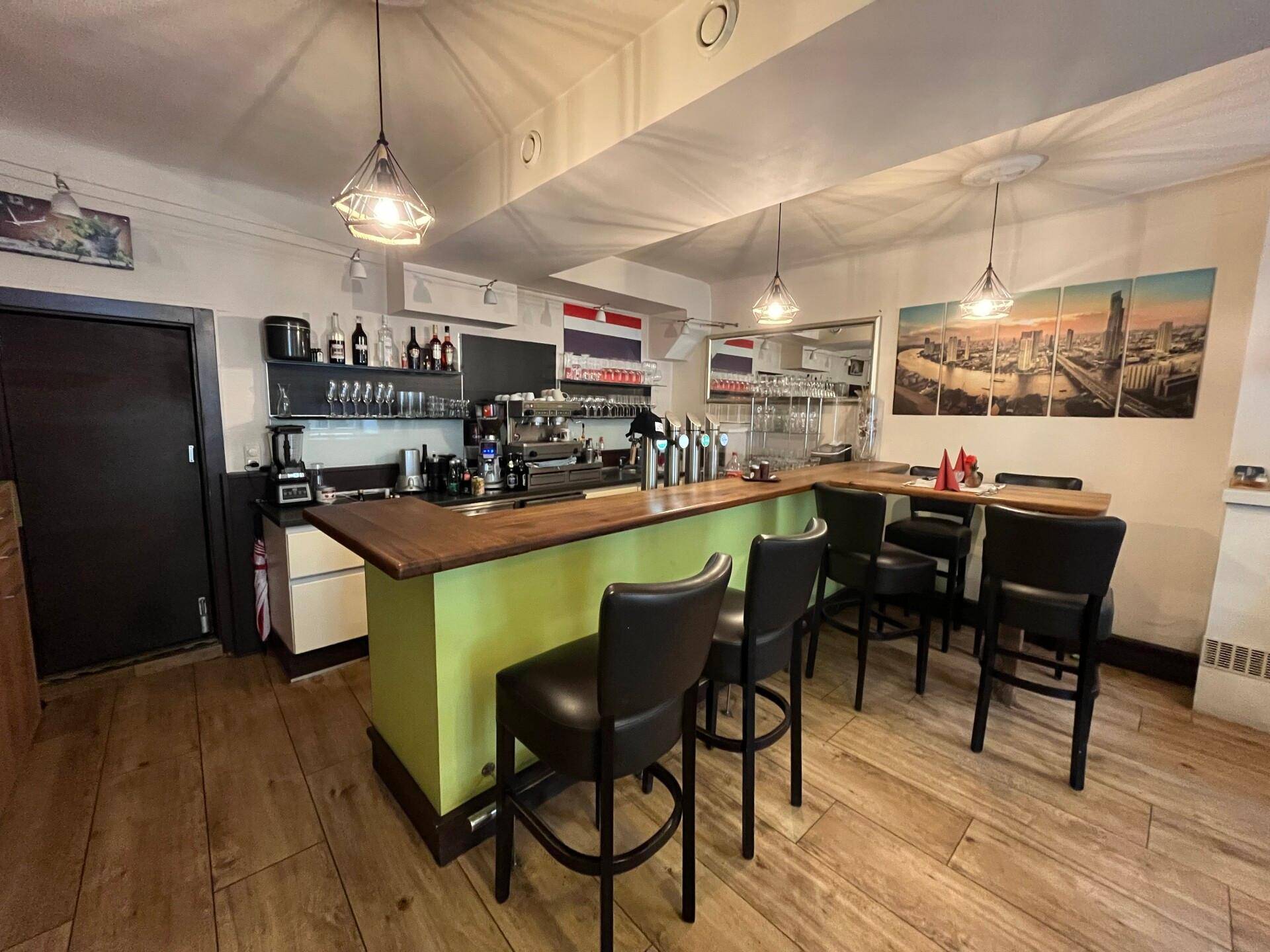 Moderne Bar mit Holztheke, Barhockern und Regalen für Getränke, ausgestattet mit einer Kaffeemaschine.