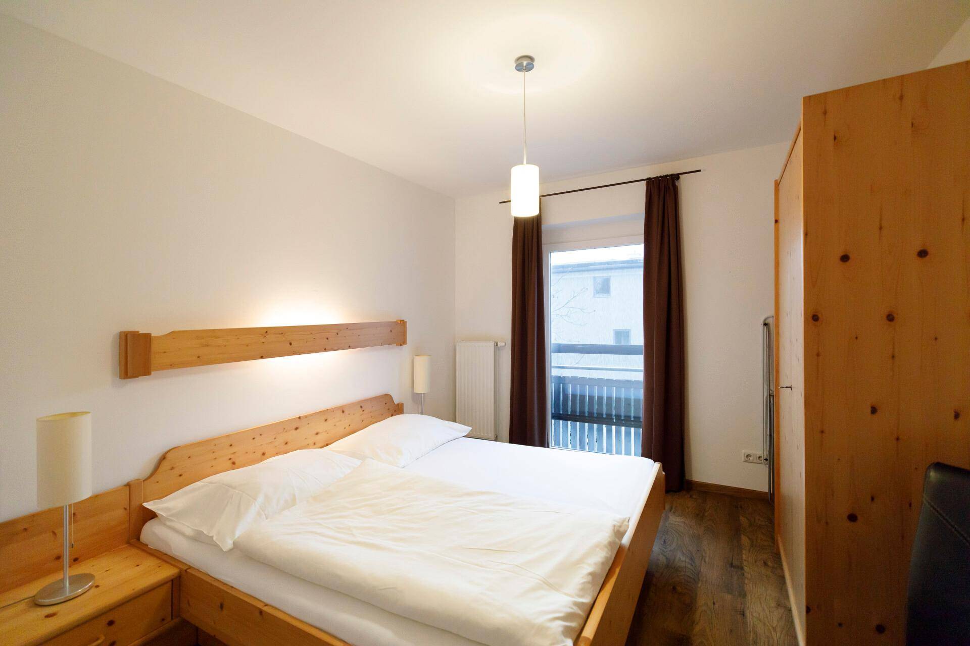 Schlafzimmer mit hellem Holzdoppelbett, Holzschrank und Zugang zu einem Balkon.