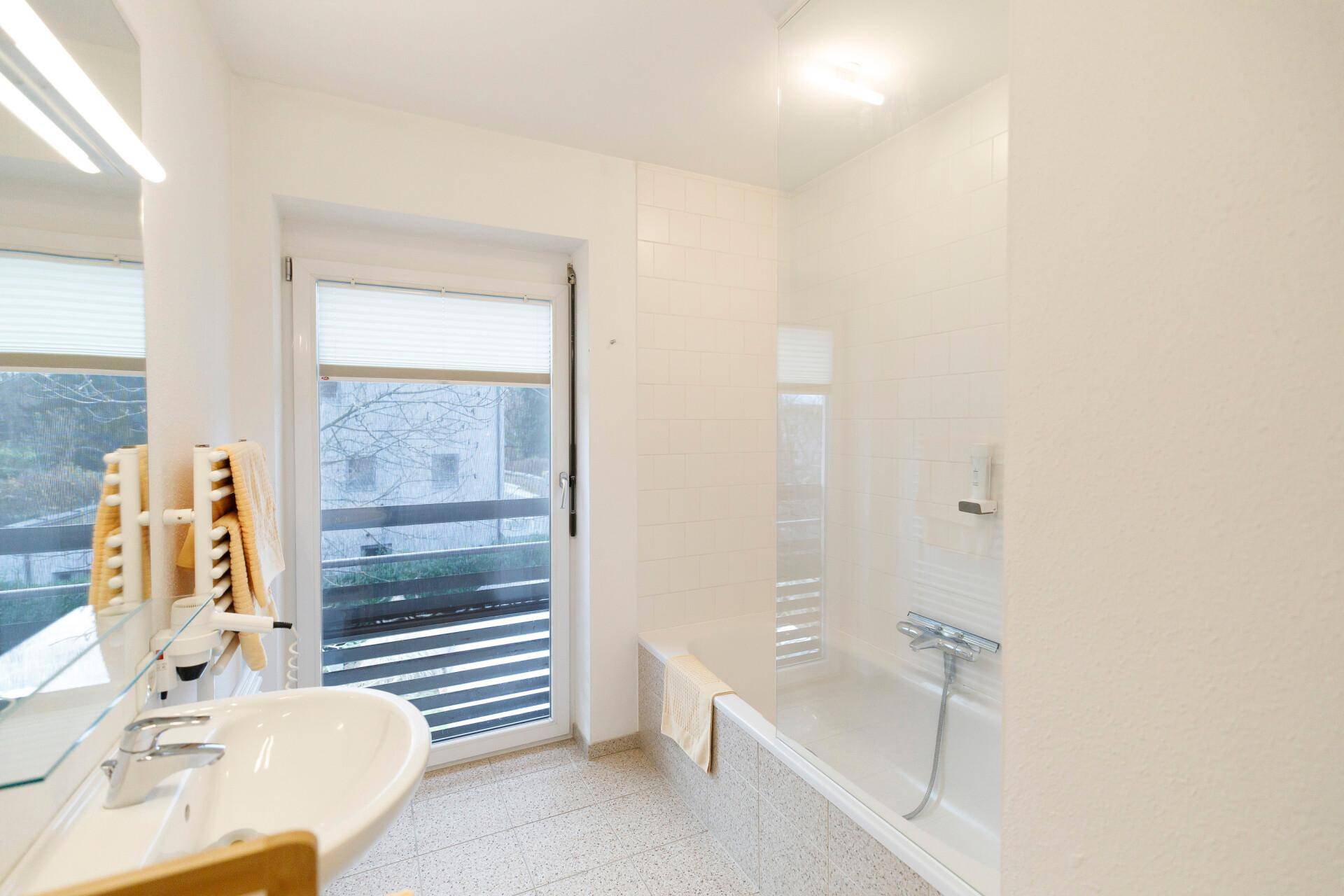 Helles Badezimmer mit Badewanne, Waschbecken und Fenster, das viel Tageslicht hereinlässt.