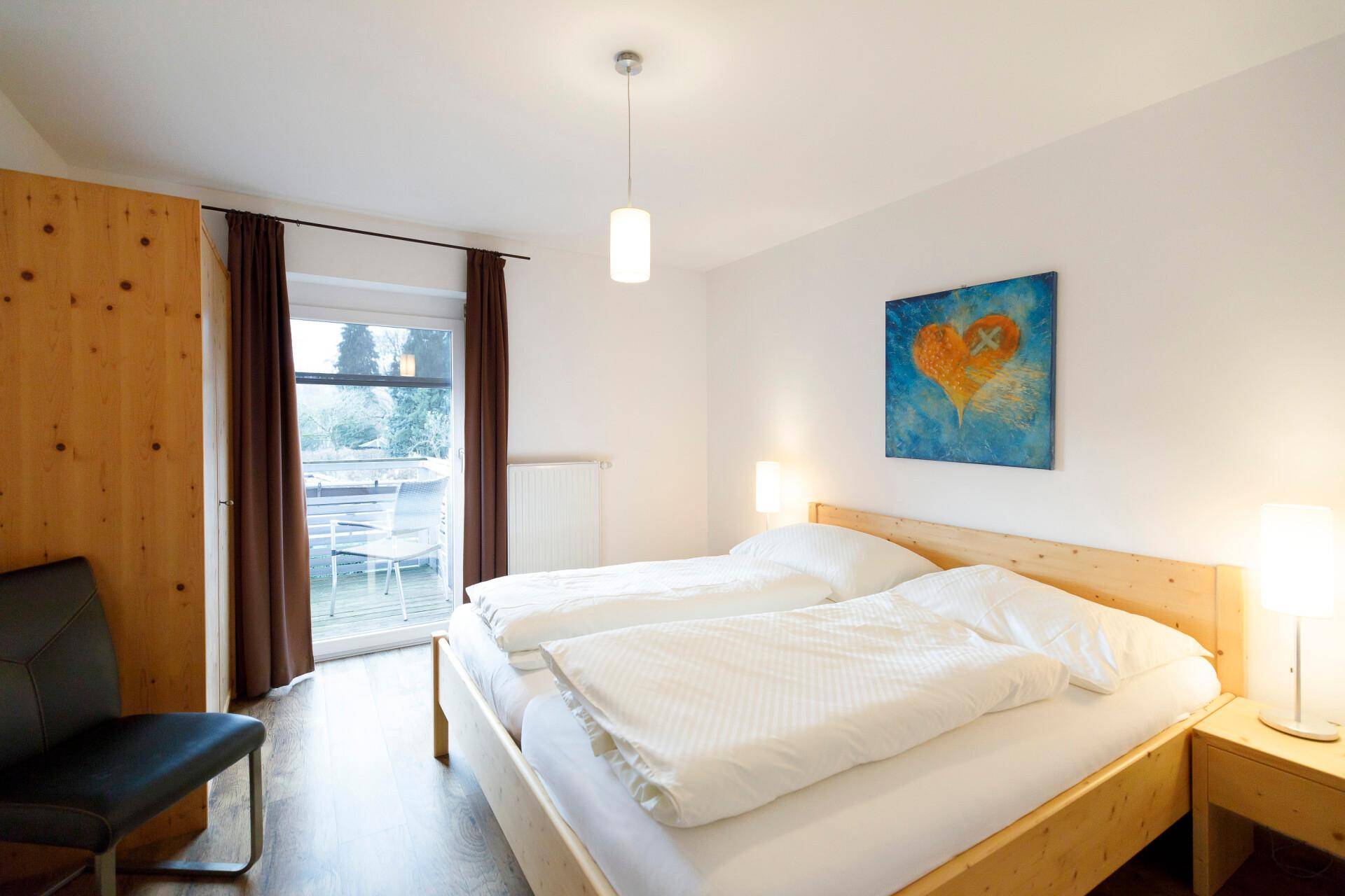 Helles Schlafzimmer mit Doppelbett, Holzboden und Balkonzugang, dekoriert mit einem modernen Bild.