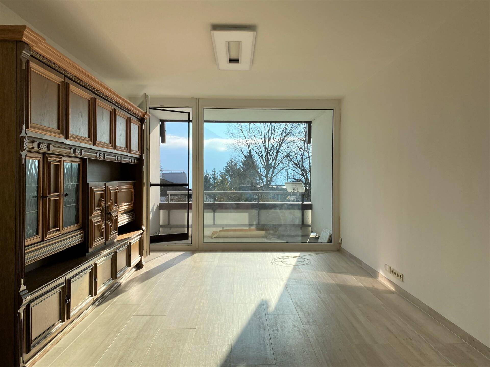 Geräumiger Wohnbereich mit großem Fenster und Balkonzugang, der viel Tageslicht hereinlässt.