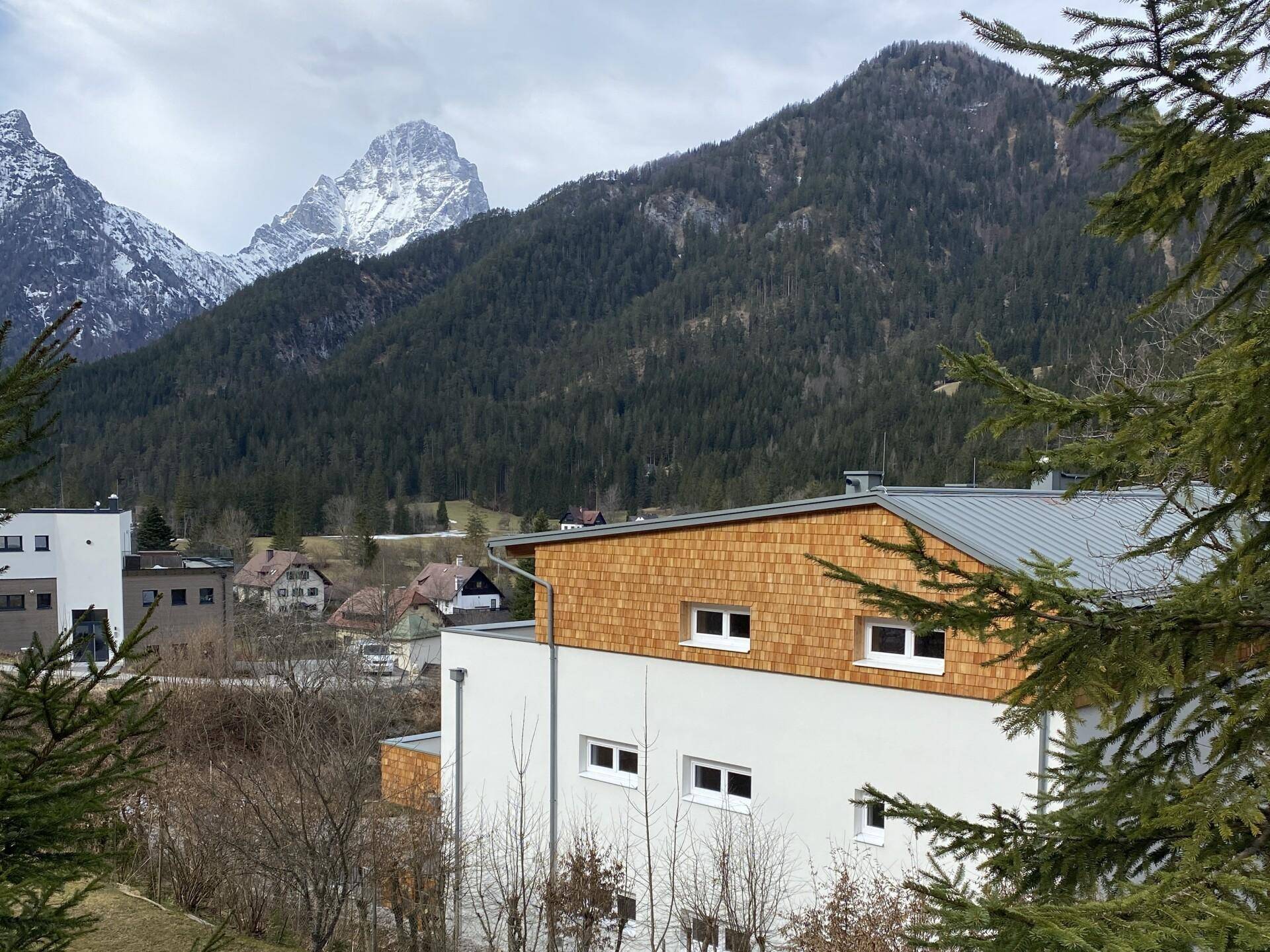 Seitenansicht eines modernen Gebäudes mit Holzfassade vor einer beeindruckenden Bergkulisse.