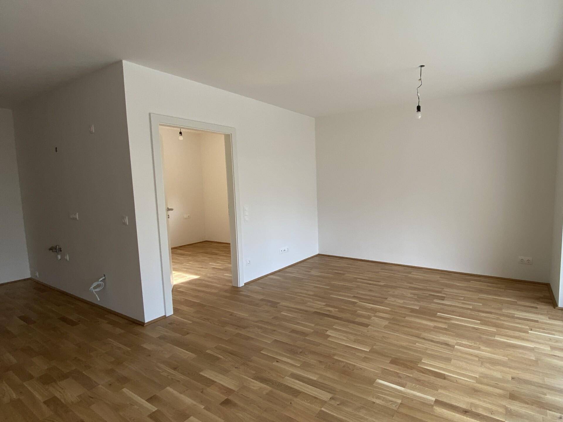 Geräumiger, unmöblierter Raum mit hellem Parkettboden und weißen Wänden, bereit zum Einzug.