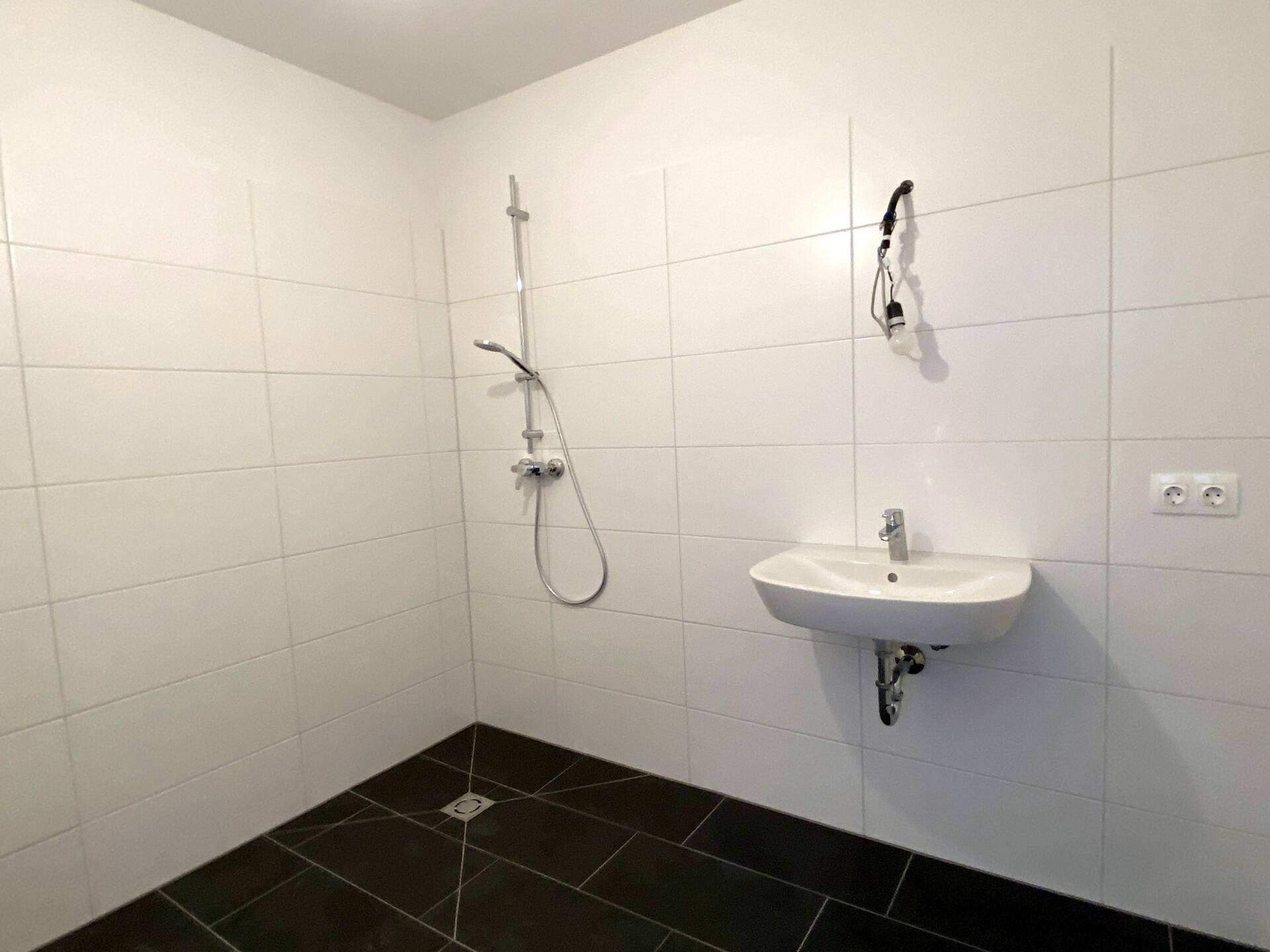 Modernes Badezimmer mit weißen Wandfliesen, dunklem Boden und einer ebenerdigen Dusche.