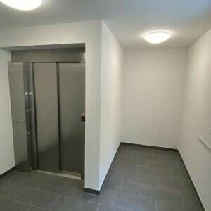 Heller Flur mit modernem Aufzug und Fliesenboden in neutralen Farben, der einen gepflegten Eindruck macht.