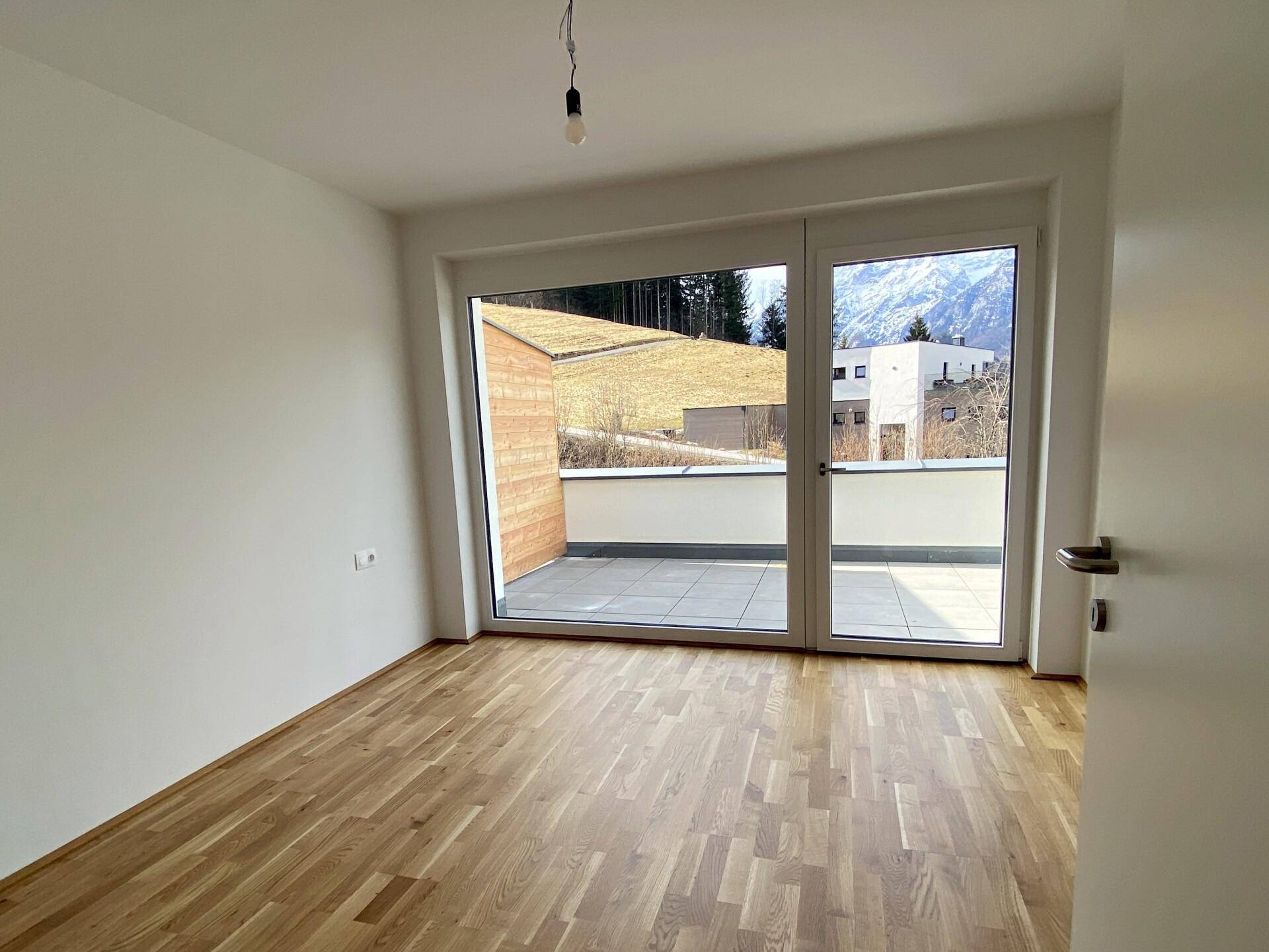 Heller, leerer Raum mit Holzboden und Zugang zu einer Terrasse mit Bergblick.