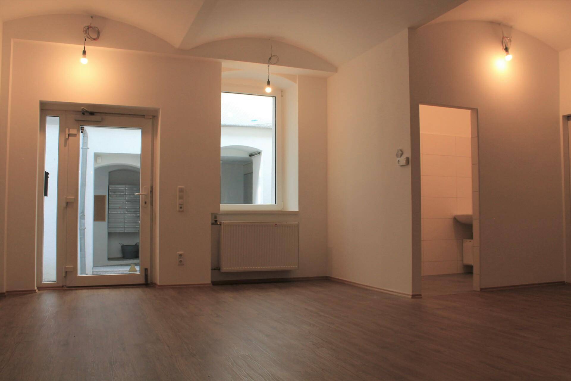 Heller, leerer Raum mit gewölbter Decke, Eingangstür und Zugang zu einem weiteren Zimmer.