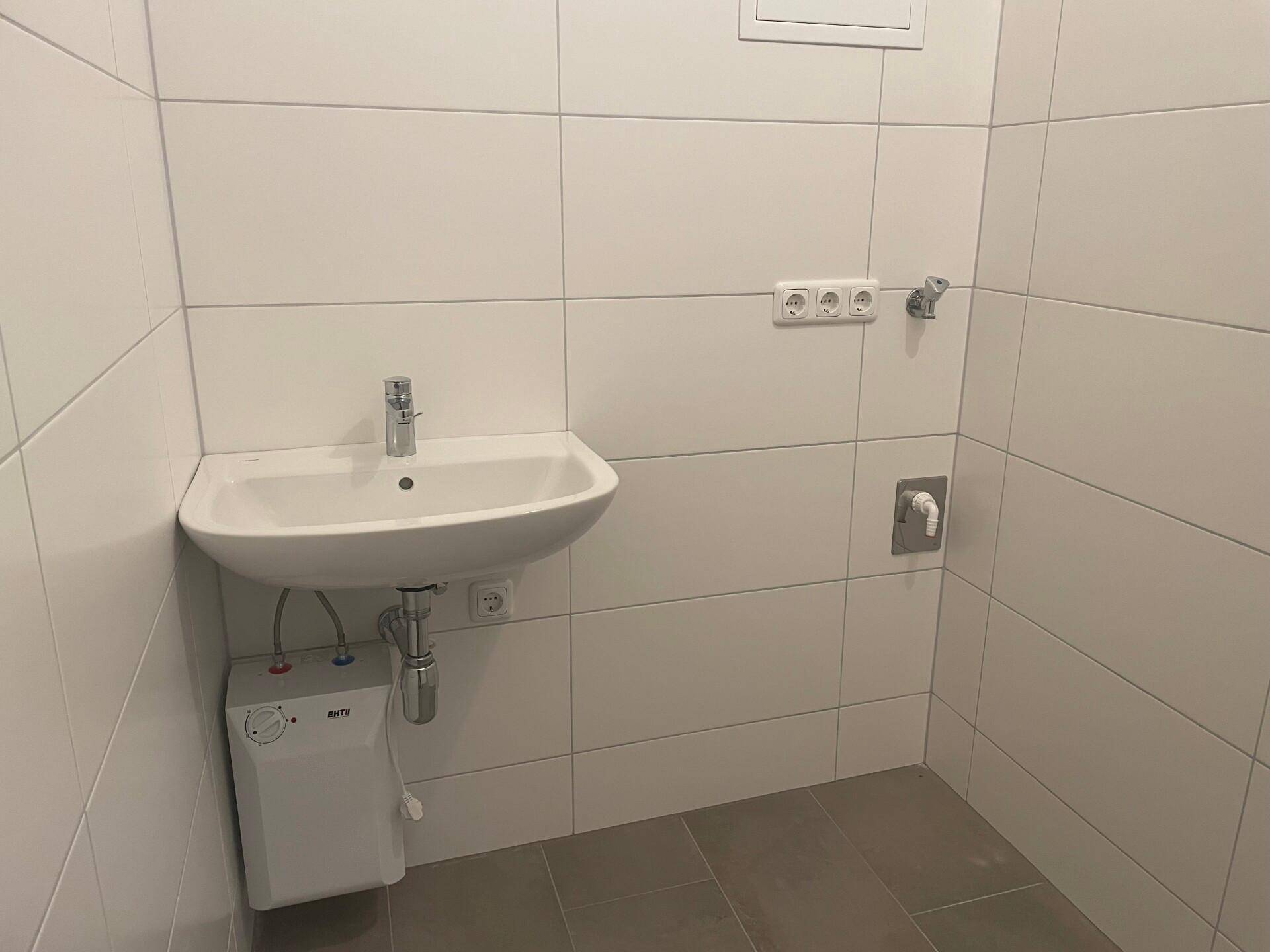 Kleines Badezimmer oder Gäste-WC mit Waschbecken, weißen Wandfliesen und grauen Bodenfliesen.
