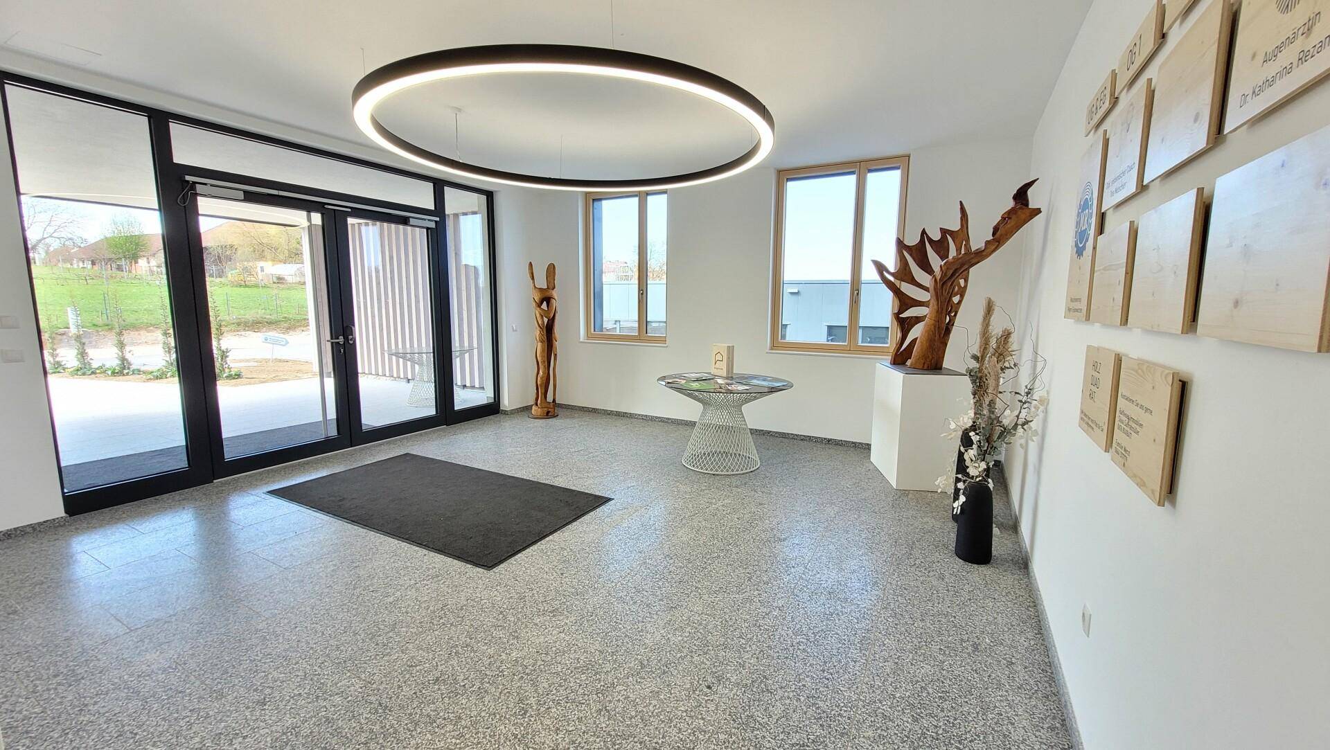 Heller, moderner Empfangsbereich mit großen Fenstern, Terrazzoboden und einer auffälligen runden Deckenleuchte.