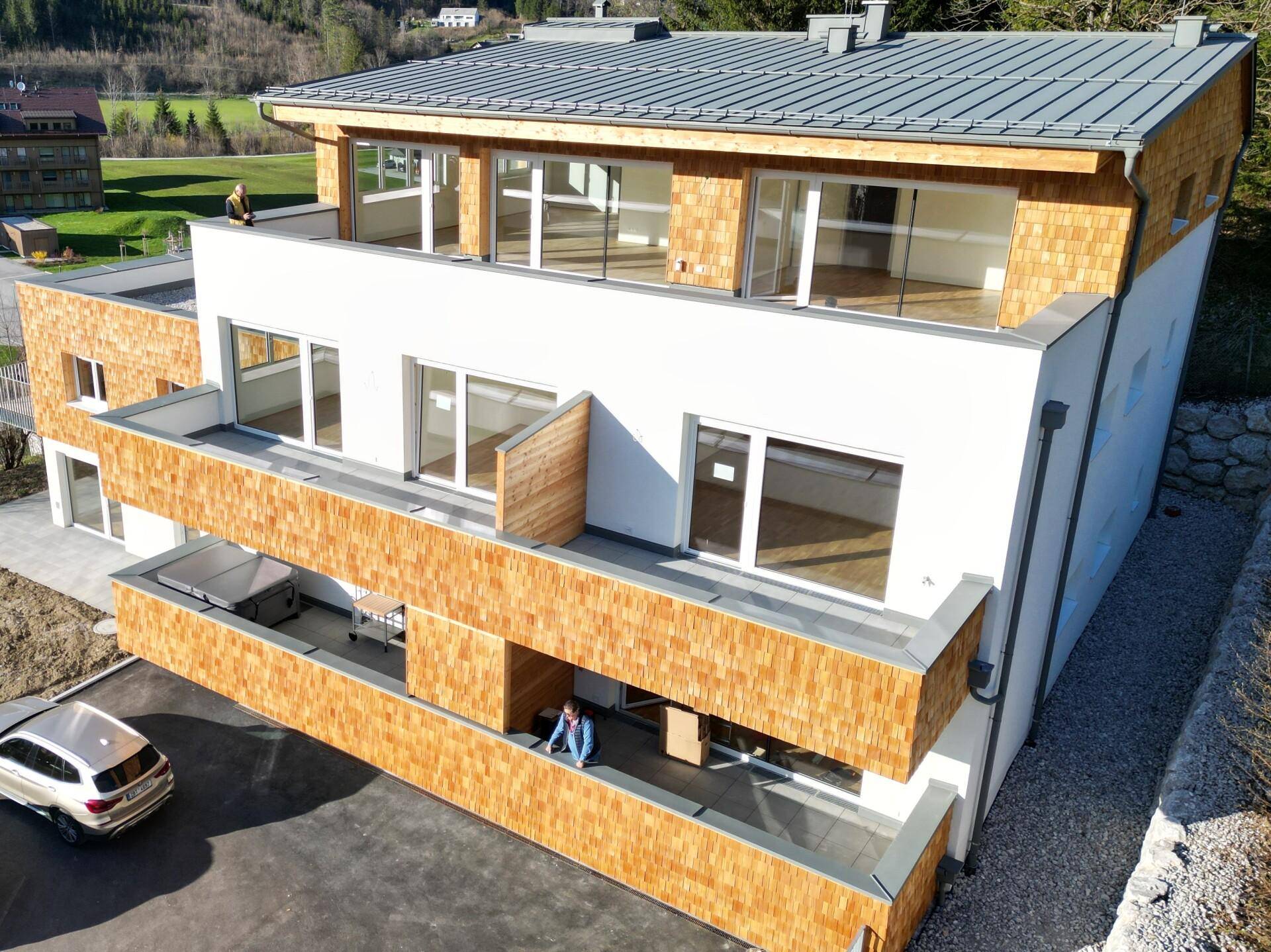 Moderne Architektur eines Neubaus mit Holzschindeln und mehreren Balkonen in alpiner Umgebung.