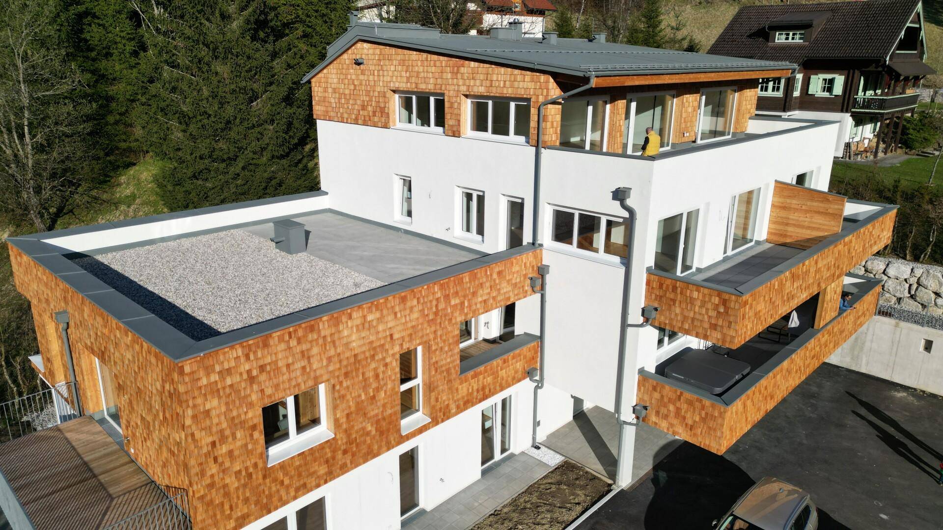 Luftaufnahme eines modernen Wohngebäudes mit mehreren Terrassen und Balkonen, umgeben von Natur.