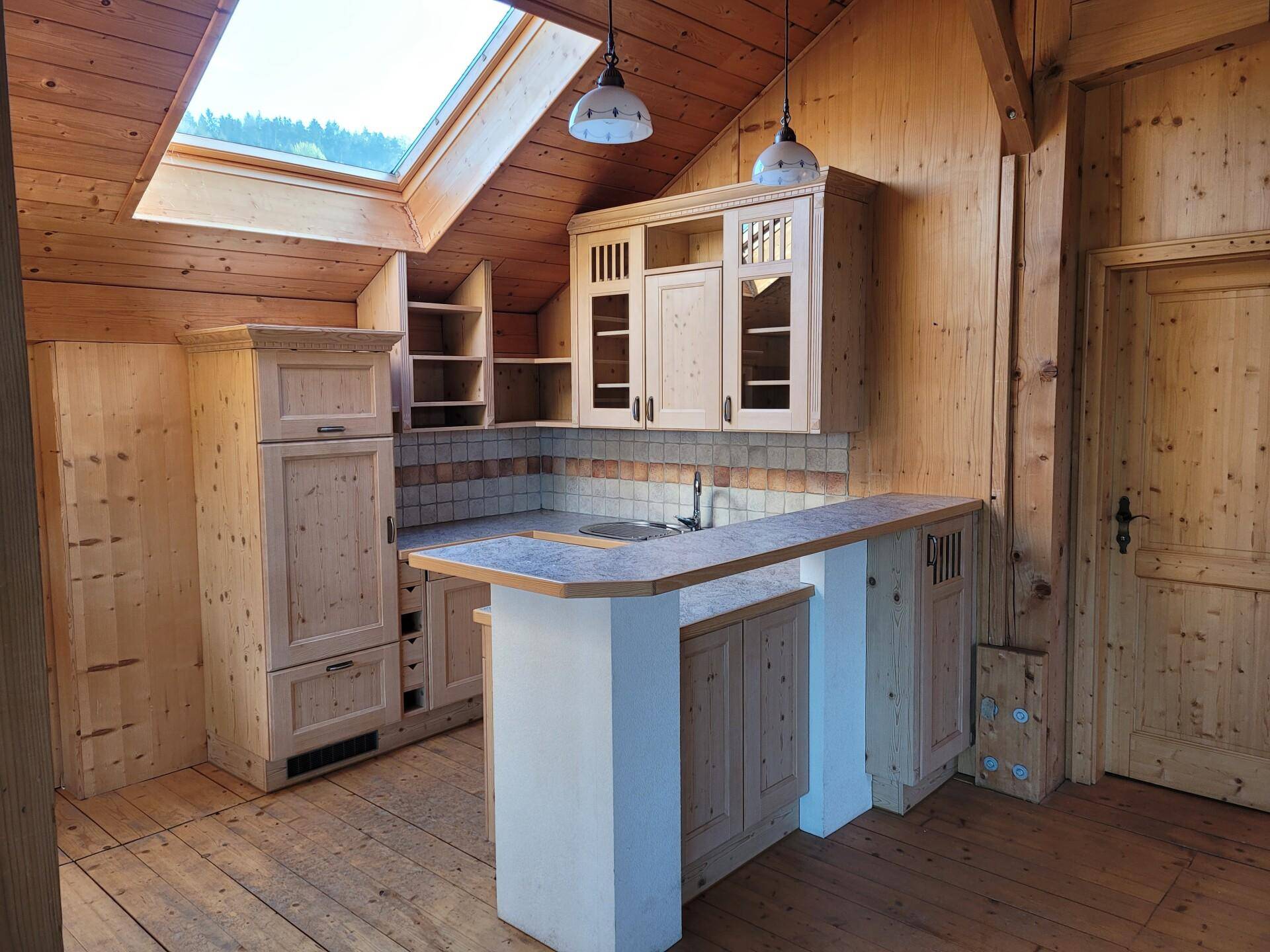 Kleine Holzküche mit hellen Schränken, Spüle und einem Dachfenster, das viel Licht hereinlässt.