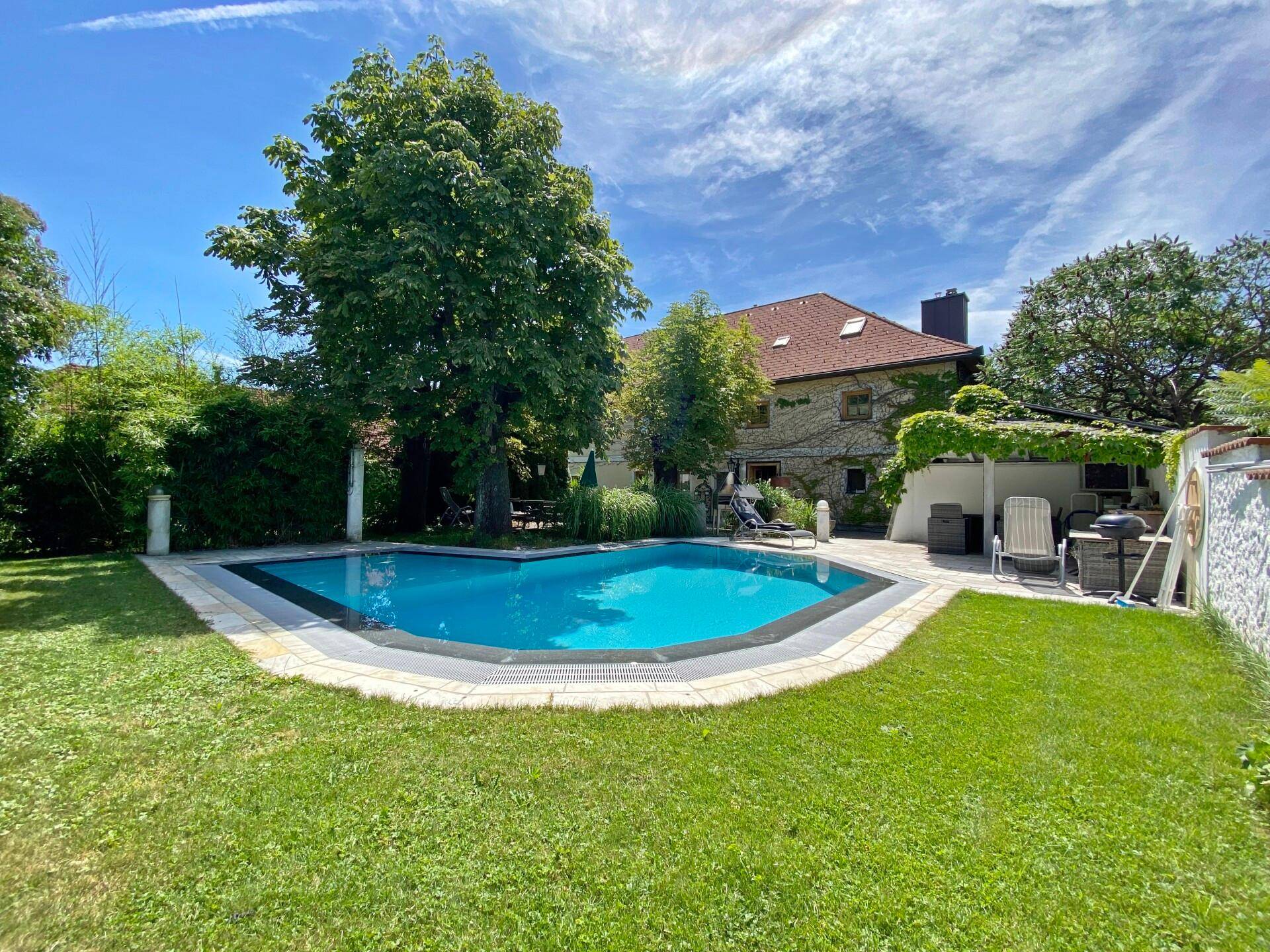 Großer Garten mit einem einladenden Pool und Liegeflächen unter blauem Himmel.