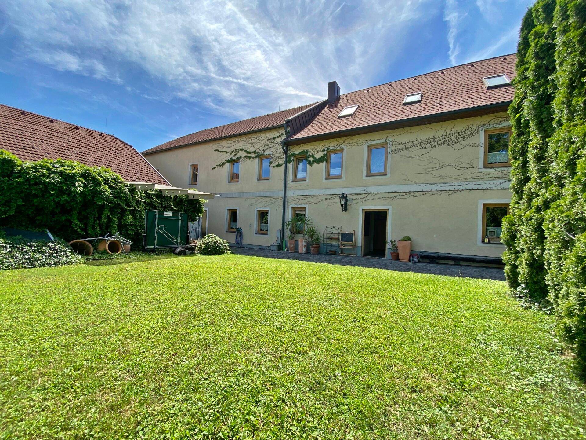 Rückseite des Gebäudes mit großem Rasen und üppiger Bepflanzung unter blauem Himmel.