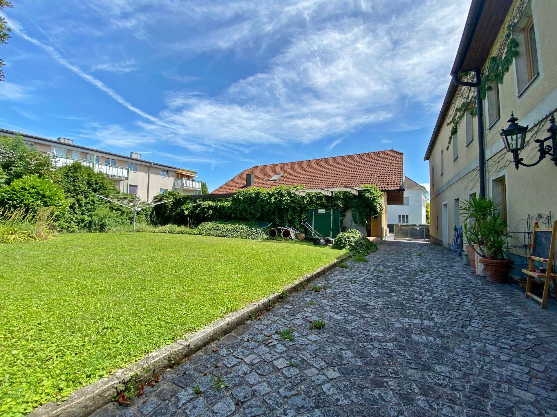Hinterhof mit großem Rasenbereich und Kopfsteinpflasterweg neben dem Gebäude.