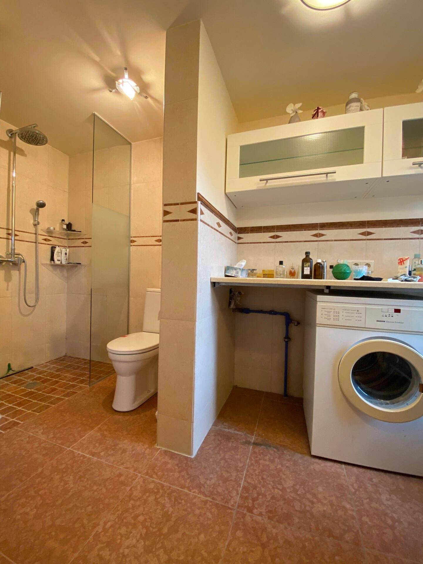 Badezimmer mit Dusche, WC und Waschmaschine, hell gefliest.