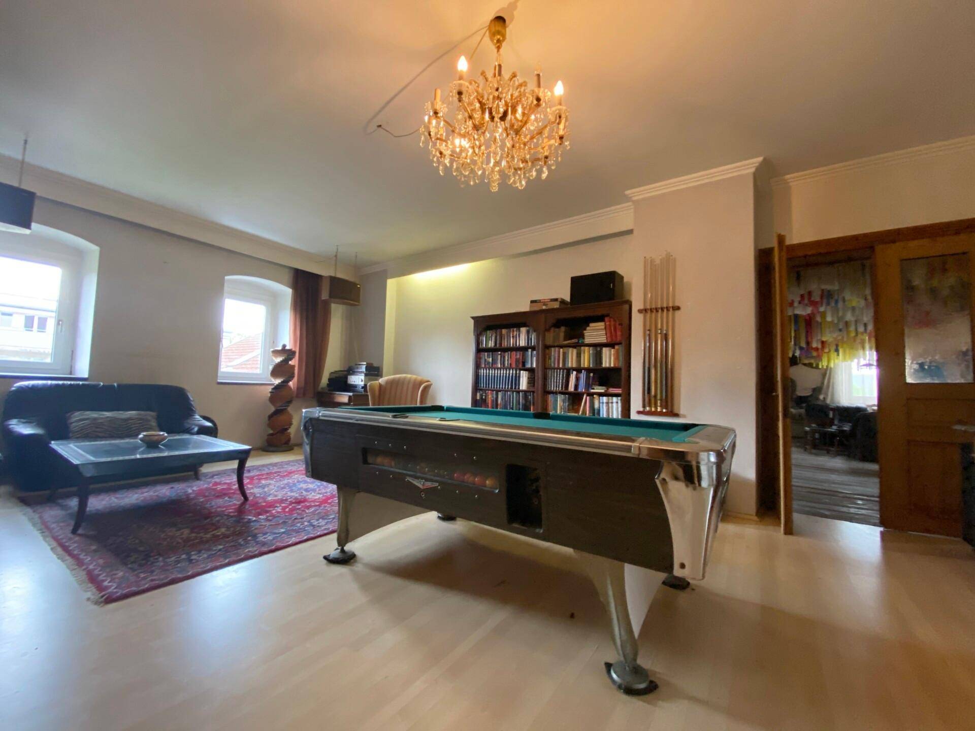 Geräumiger Raum mit Billardtisch, Bücherregal und Kronleuchter.