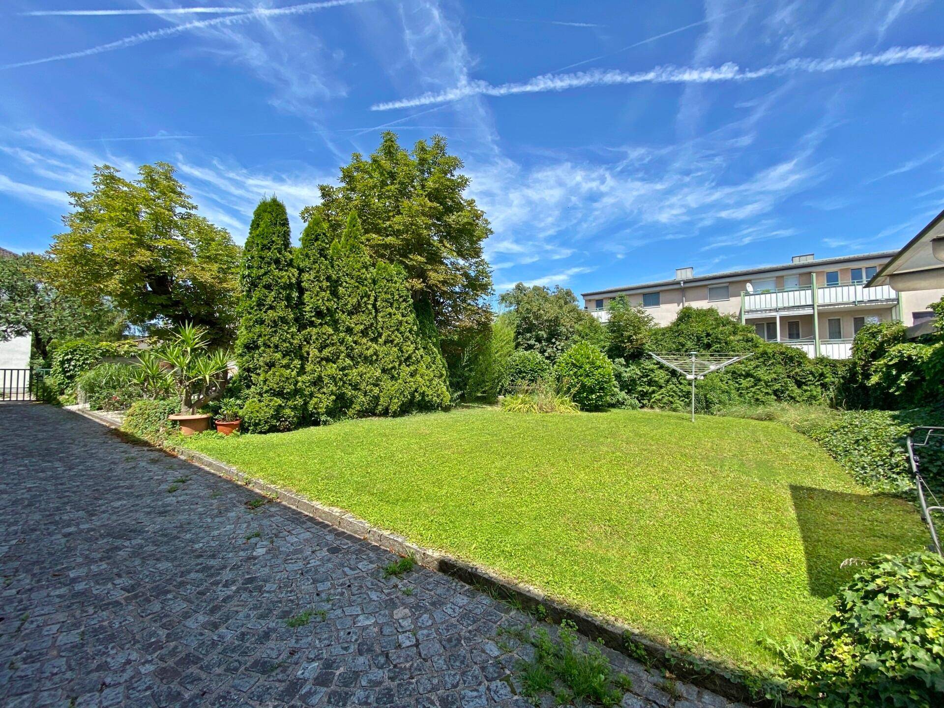 Gepflegter Gartenbereich mit Rasen, Bäumen und Blick auf umliegende Gebäude.
