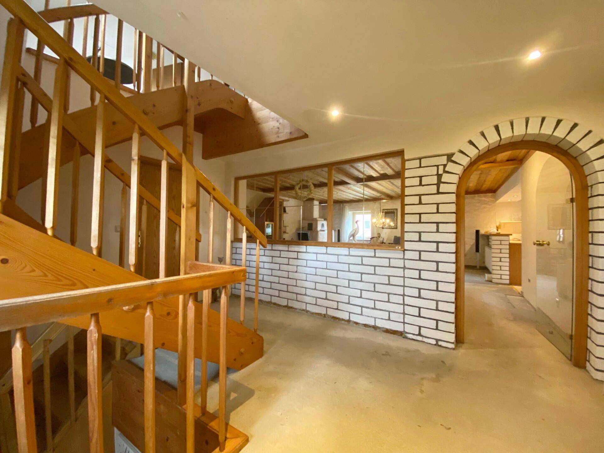 Heller Flur mit Holztreppe, weiß gestrichenen Ziegelwänden und Holzbalkendecke.