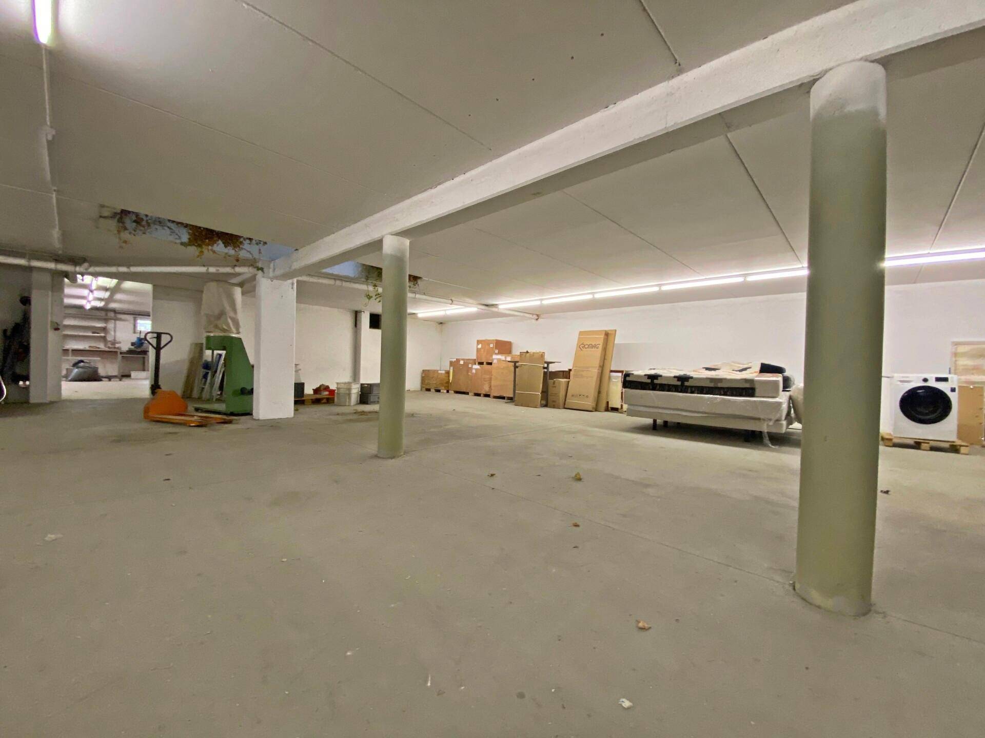 Großer Kellerraum mit Betonboden, Säulen und Lagerflächen.