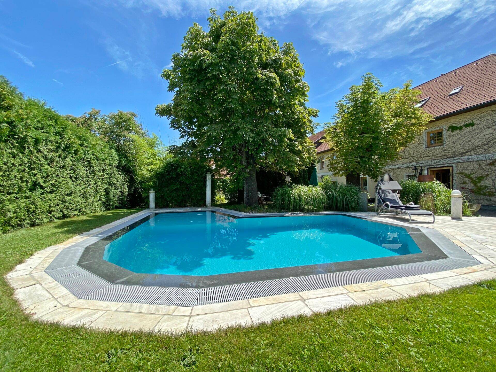 Einladender Poolbereich im Garten mit Liegestuhl und großen Bäumen.