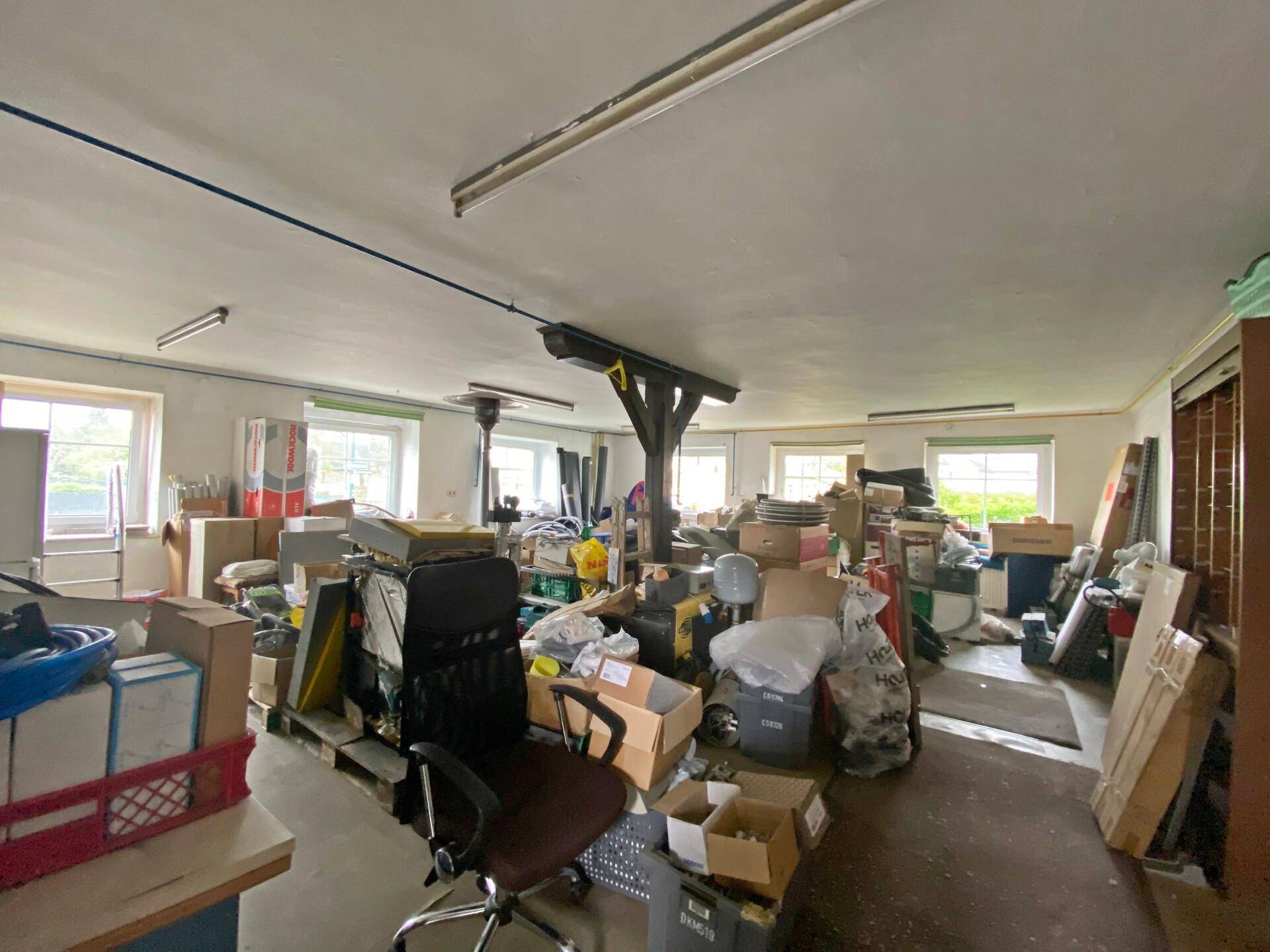 Großer Abstellraum mit vielen Kartons, Bürostuhl und Fenstern.