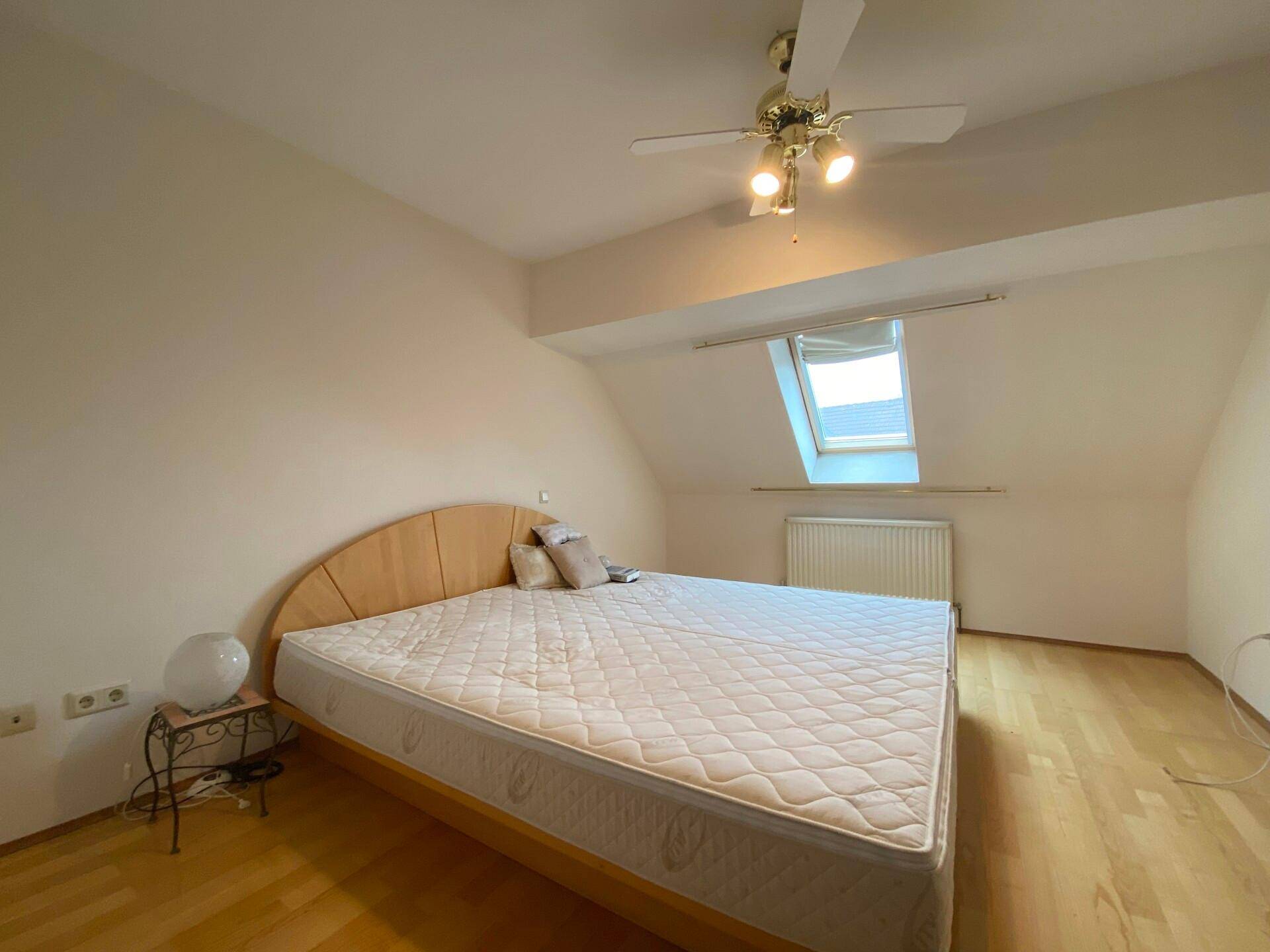 Schlafzimmer im Dachgeschoss mit Holzboden, großem Bett und Dachfenster.