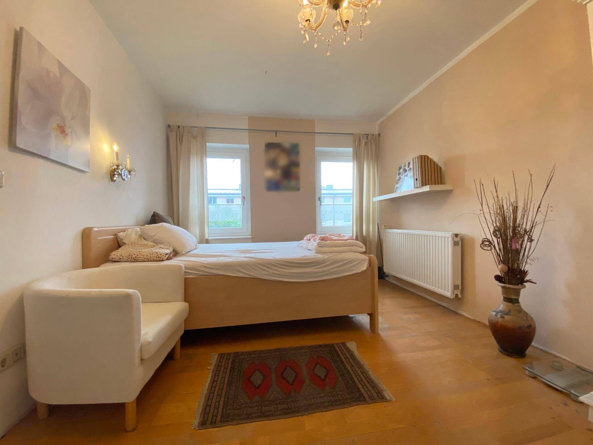 Helles Schlafzimmer mit Holzboden, großem Bett und Kronleuchter.
