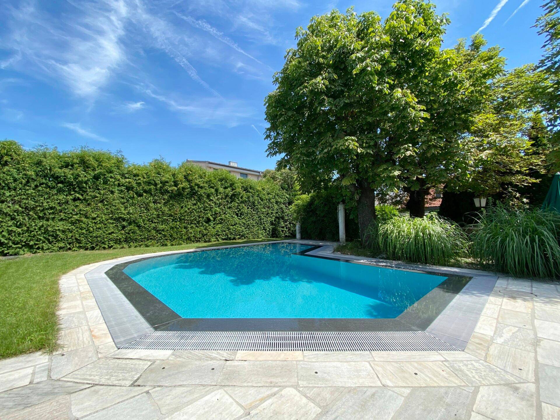 Attraktiver Poolbereich im Garten mit Steinplatten und umgebender Hecke.