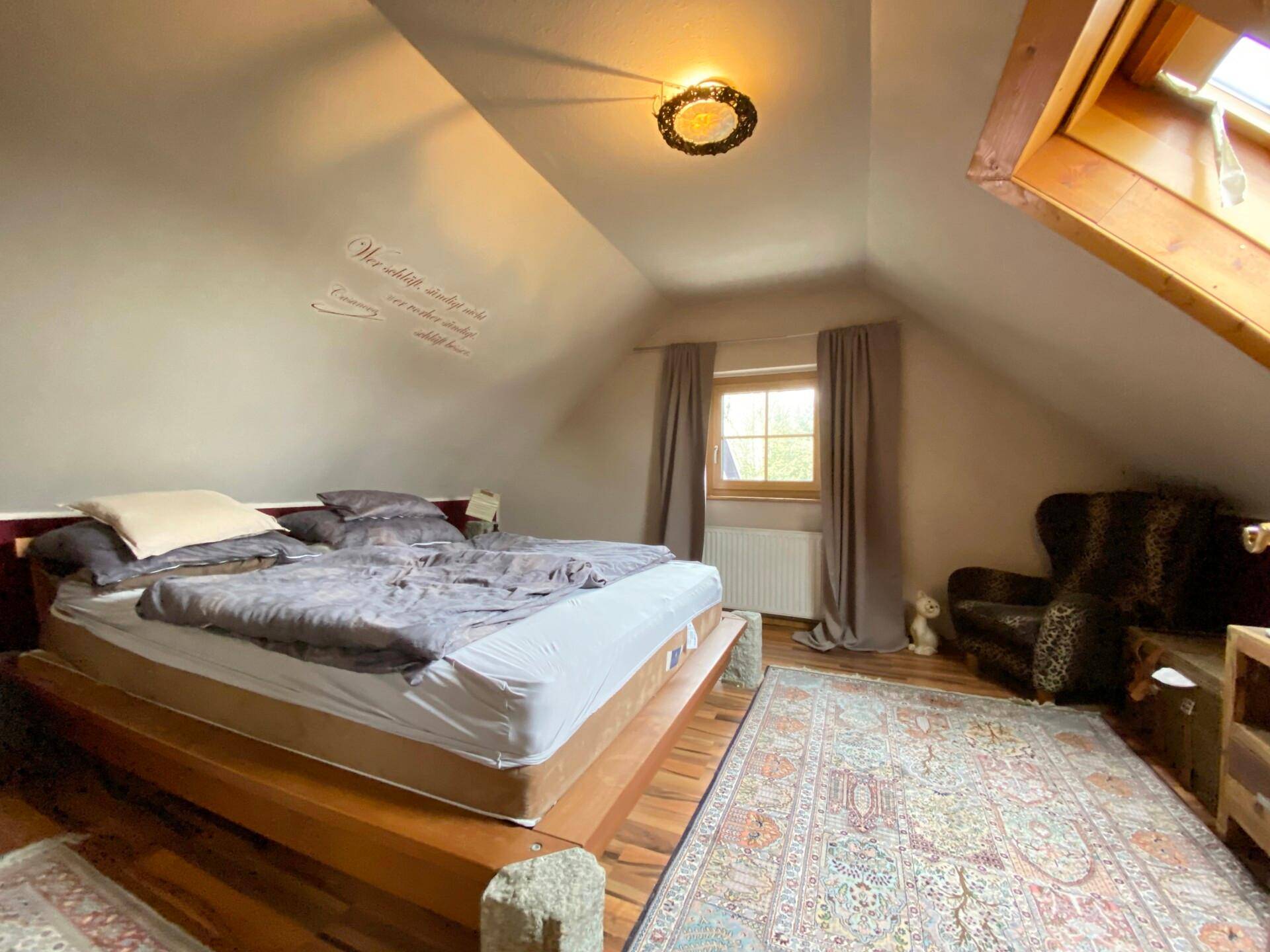 Schlafzimmer im Dachgeschoss mit Holzbett, Teppich und Dachfenster.
