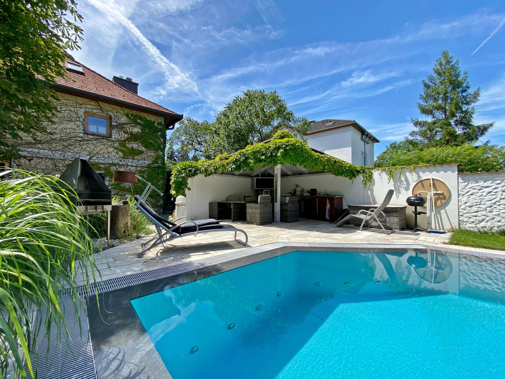 Entspannender Poolbereich mit Liegestühlen und einer überdachten Grillzone im Garten.