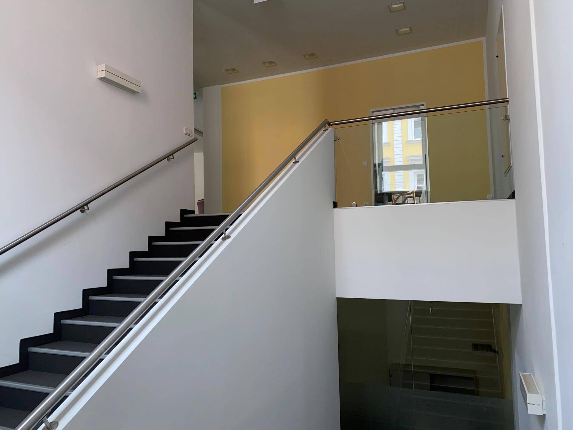 Modernes Treppenhaus mit Edelstahlgeländer und Glasbrüstung, das zu den oberen Etagen des Gebäudes führt.