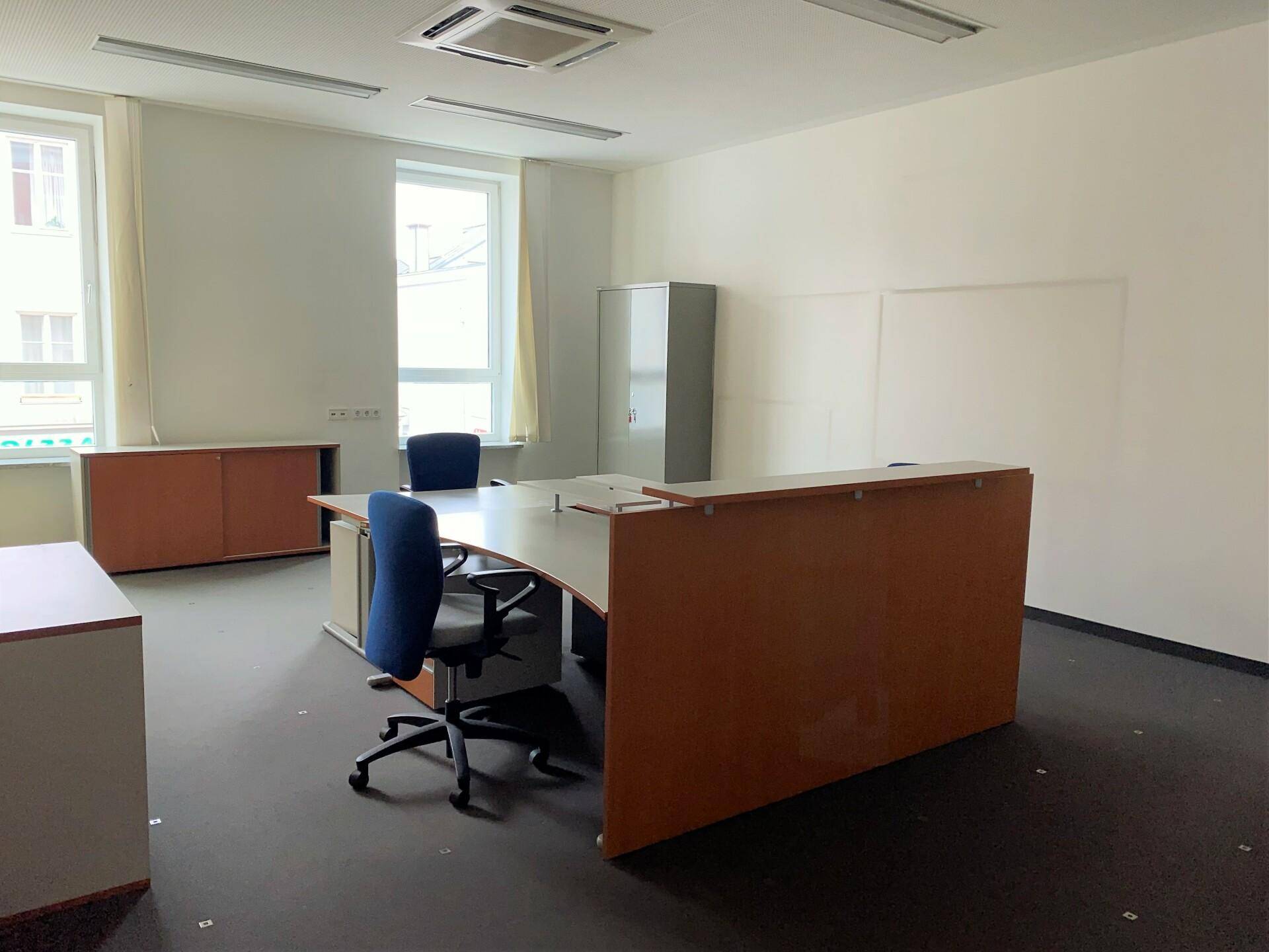 Geräumiger Büroraum mit mehreren Schreibtischen und Büroschränken, gut beleuchtet durch große Fenster.