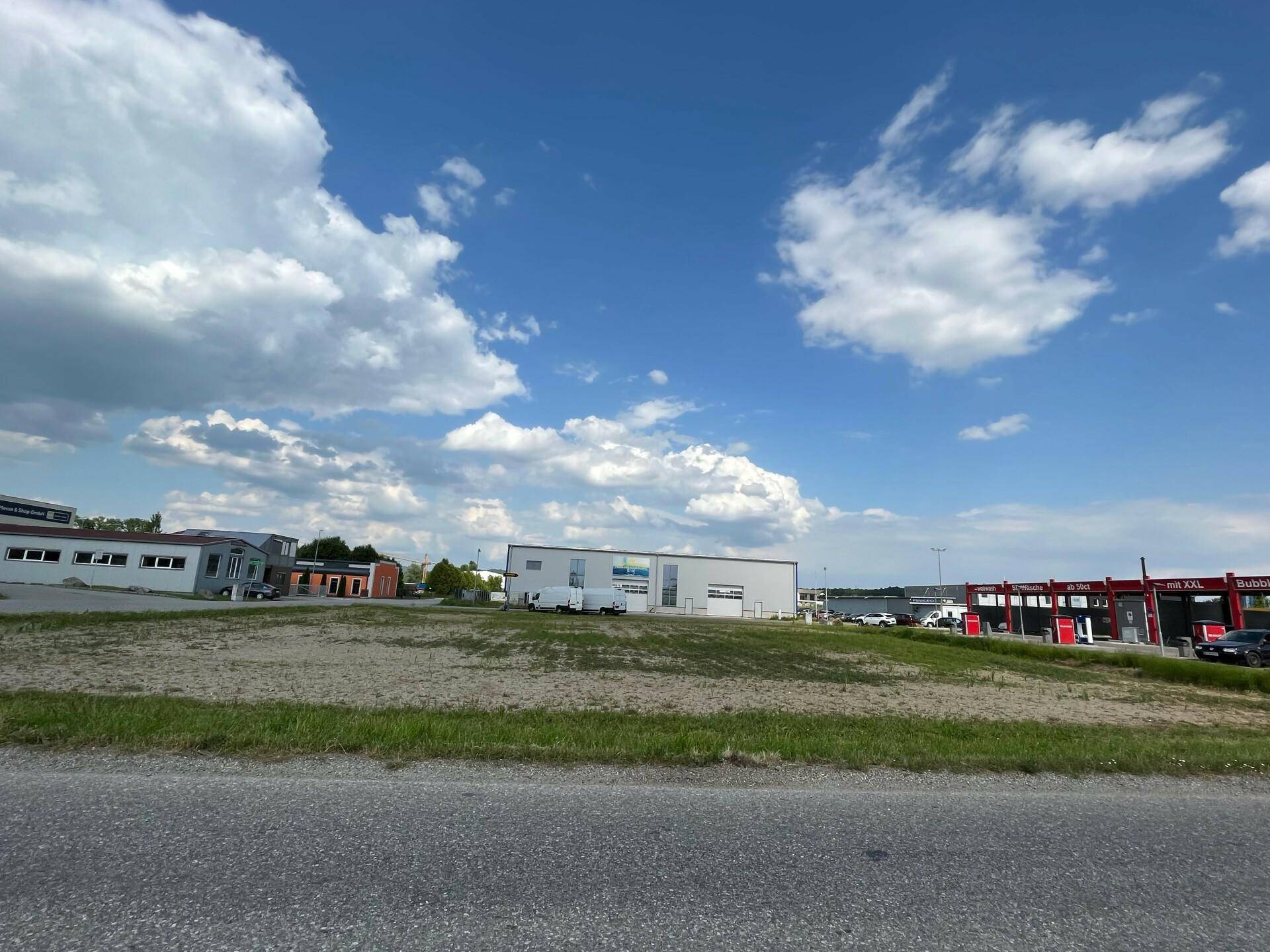 Offenes, unbebautes Grundstück mit Blick auf verschiedene Gewerbegebäude und eine Autowaschanlage in der Ferne.