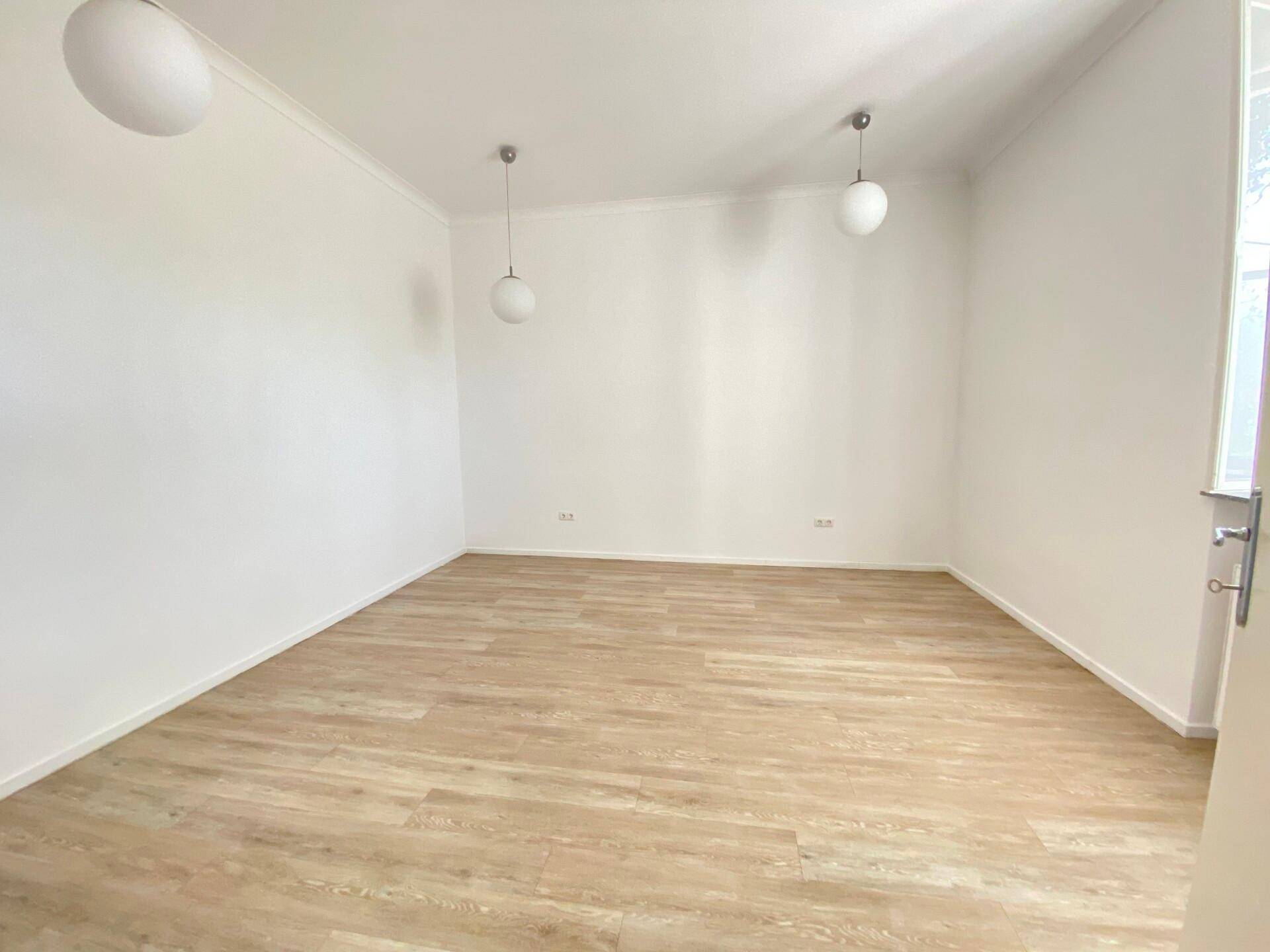 Geräumiger, leerer Raum mit hellem Laminatboden und weißen Wänden, bereit zur individuellen Einrichtung.