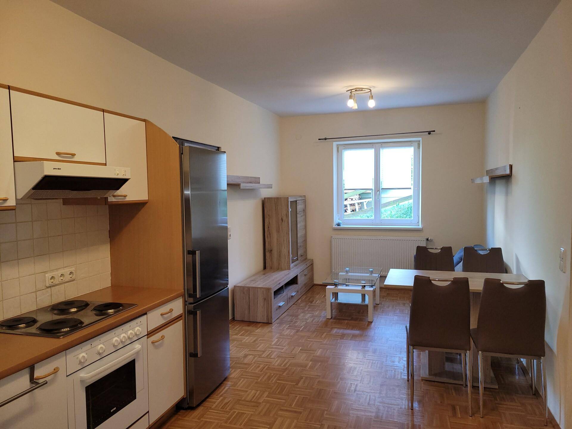 Offener Wohn- und Essbereich mit integrierter Küche, Parkettboden und einem Fenster.
