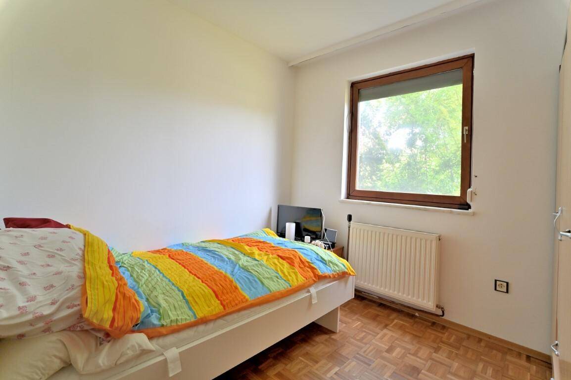 Helles Schlafzimmer mit Einzelbett, farbenfroher Bettdecke und Blick ins Grüne.