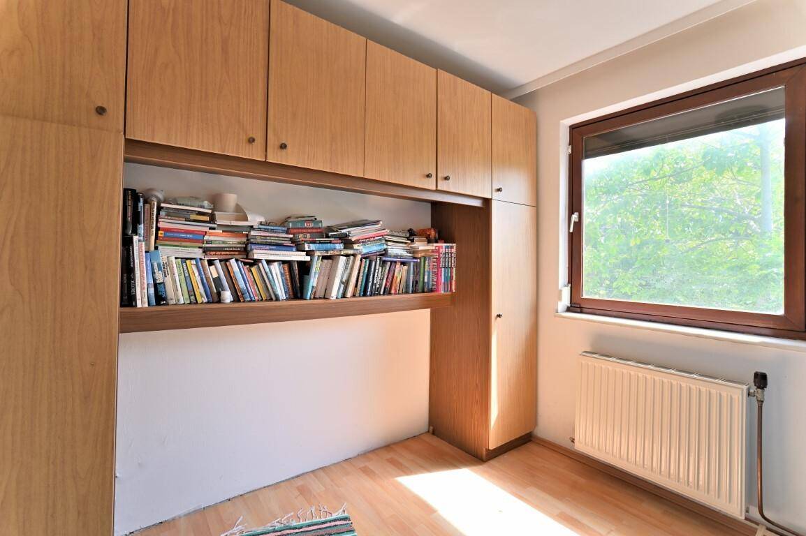 Funktionaler Raum mit eingebauten Holzschränken, Bücherregal und Fenster mit Tageslicht.
